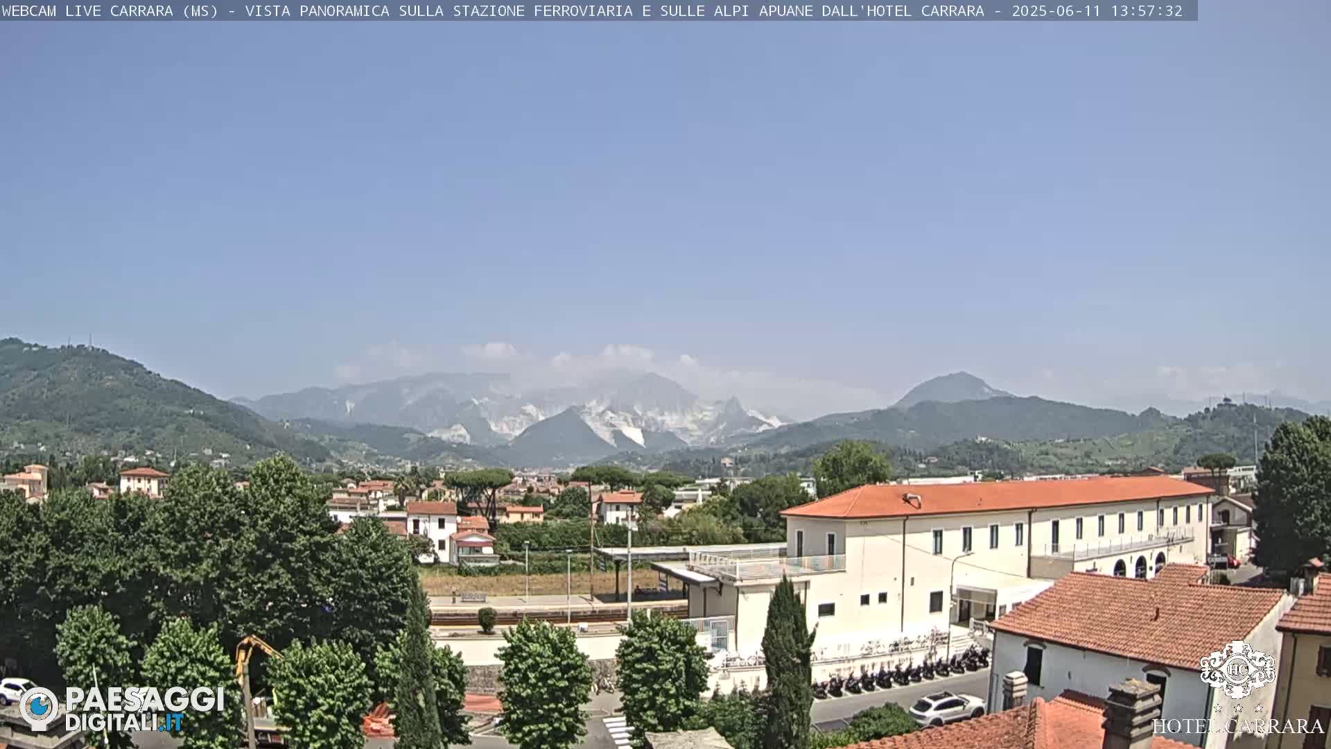 A long shot of a town nestled in a valley, under a clear blue sky, with mountains in the background.