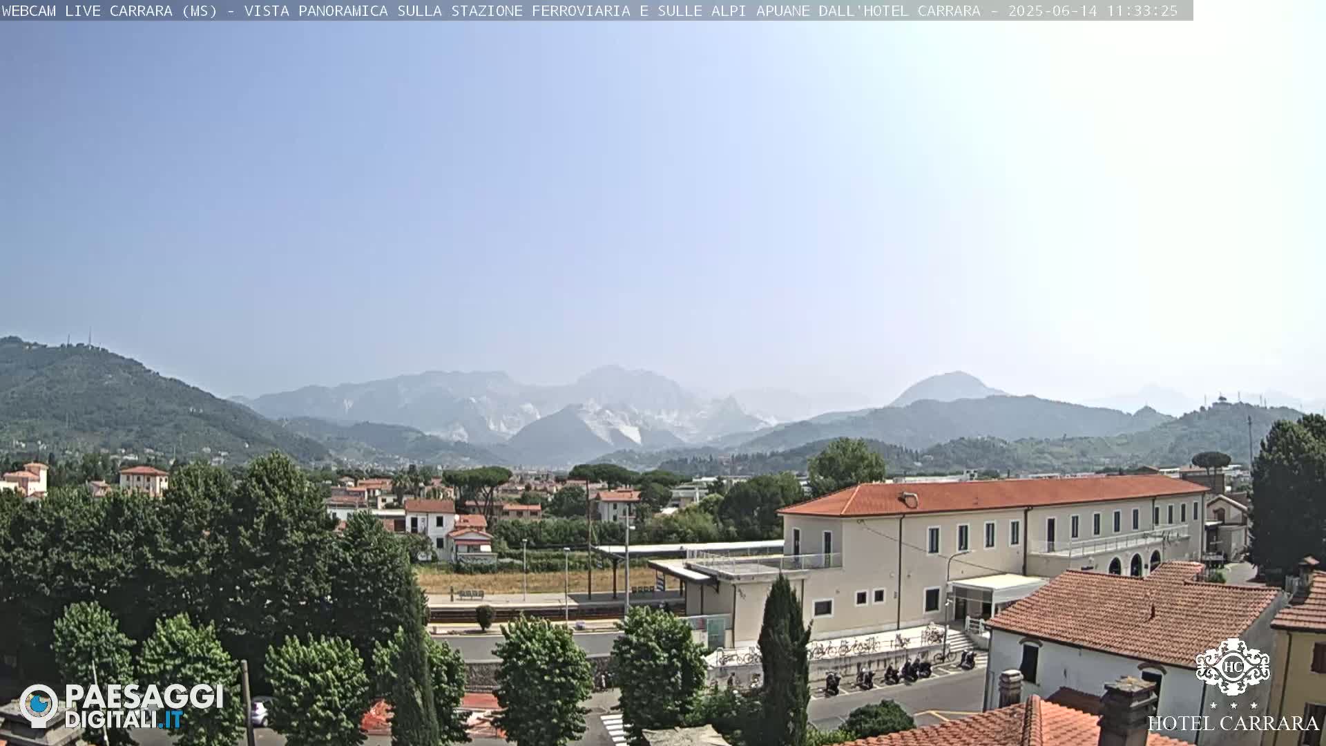 A long shot of a town nestled in a valley, with mountains in the background under a clear, sunny sky.