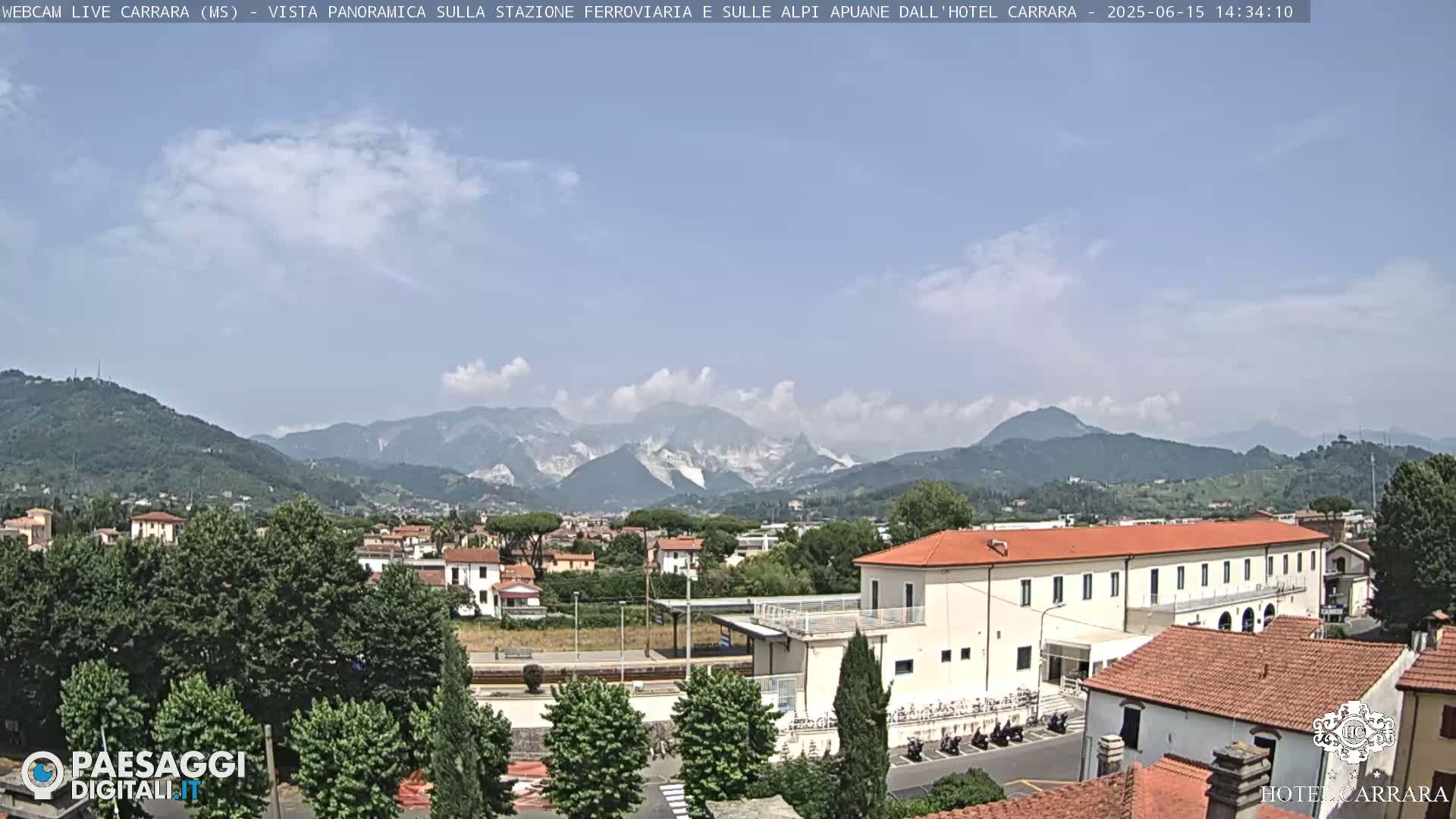 A long, low building is situated in a town nestled at the foot of a mountain range under a mostly clear, bright sky.