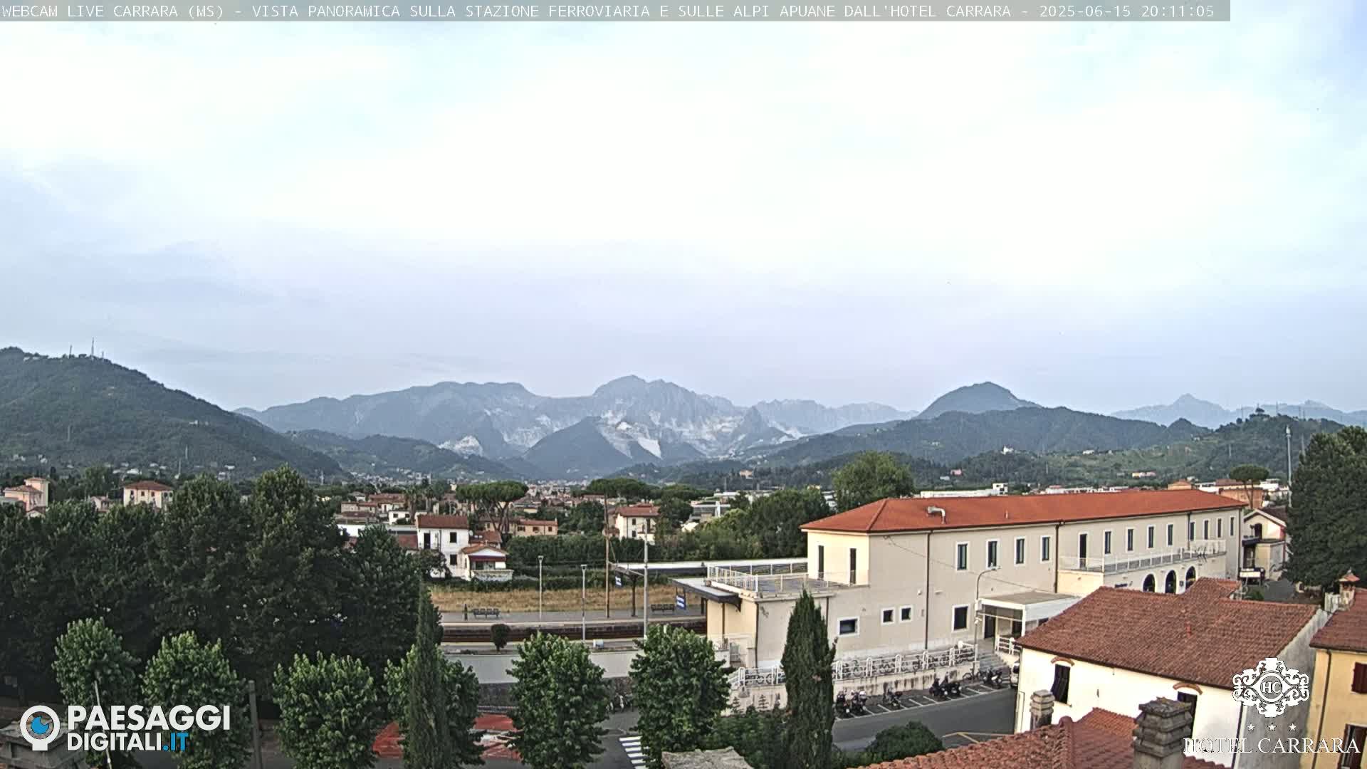 A long shot of a town nestled in a valley, overlooked by mountains under a hazy sky.