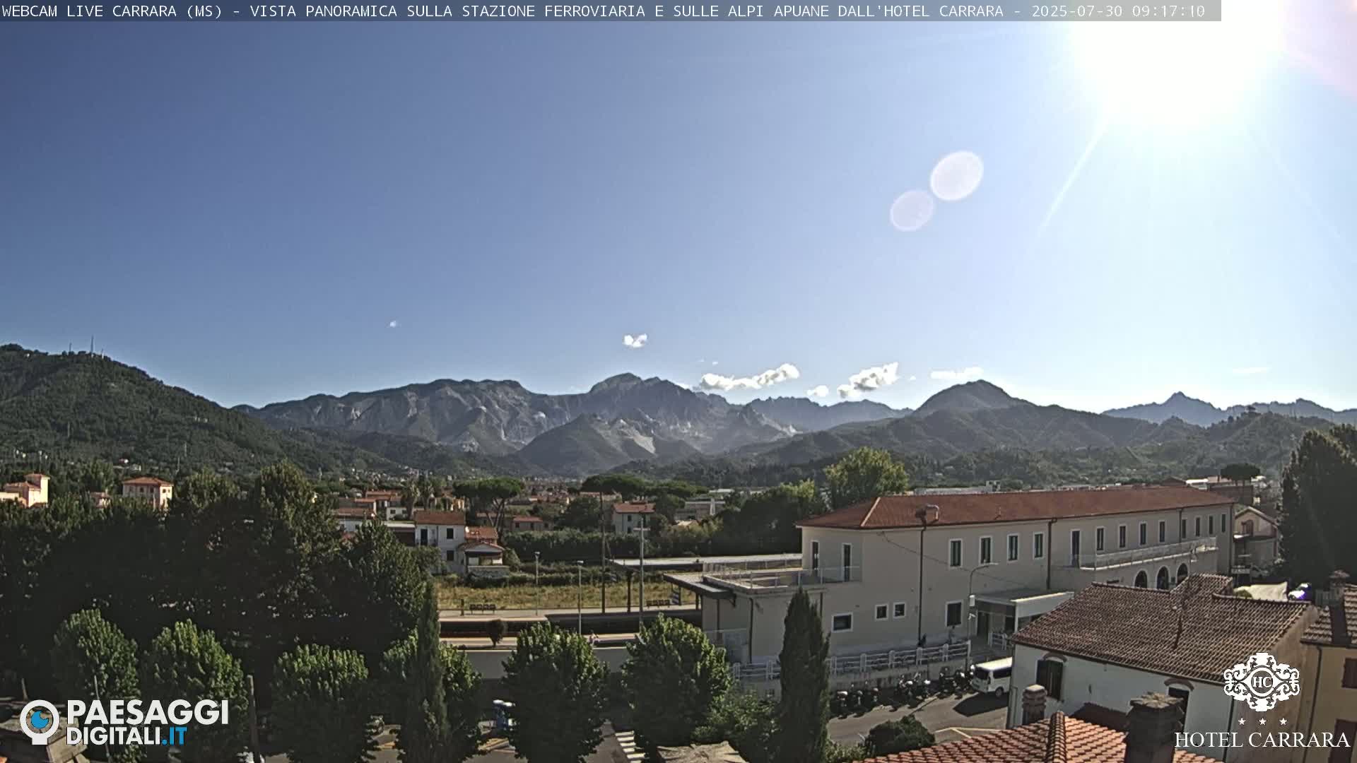 A sunny, clear day reveals a panoramic view of a town nestled in a valley, with mountains in the background.
