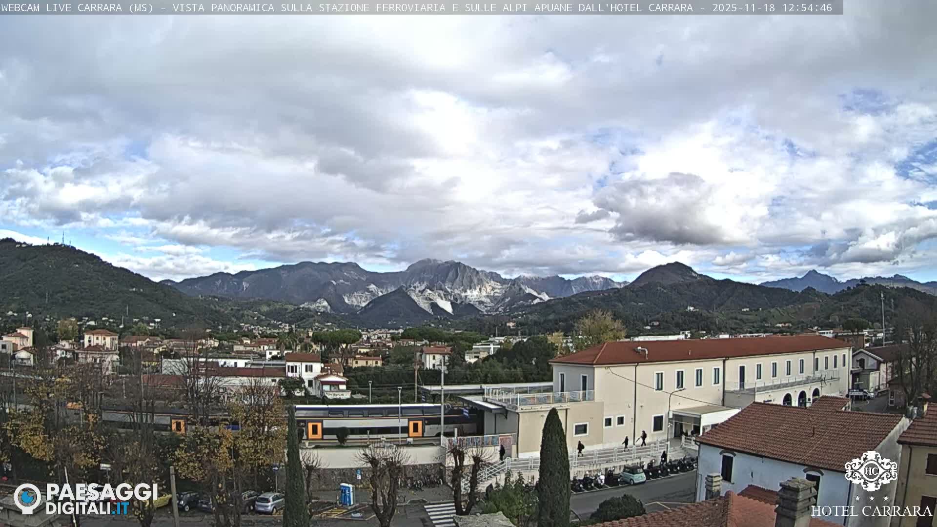 The image displays a clear night view of a town with illuminated buildings, streetlights, and a distant mountain range under a dark sky.