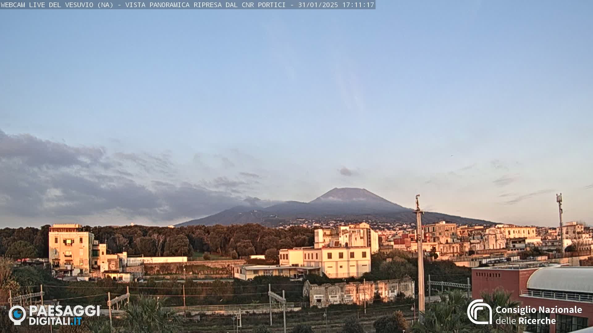 A partly cloudy sunset illuminates a cityscape and Mount Vesuvius in the distance.