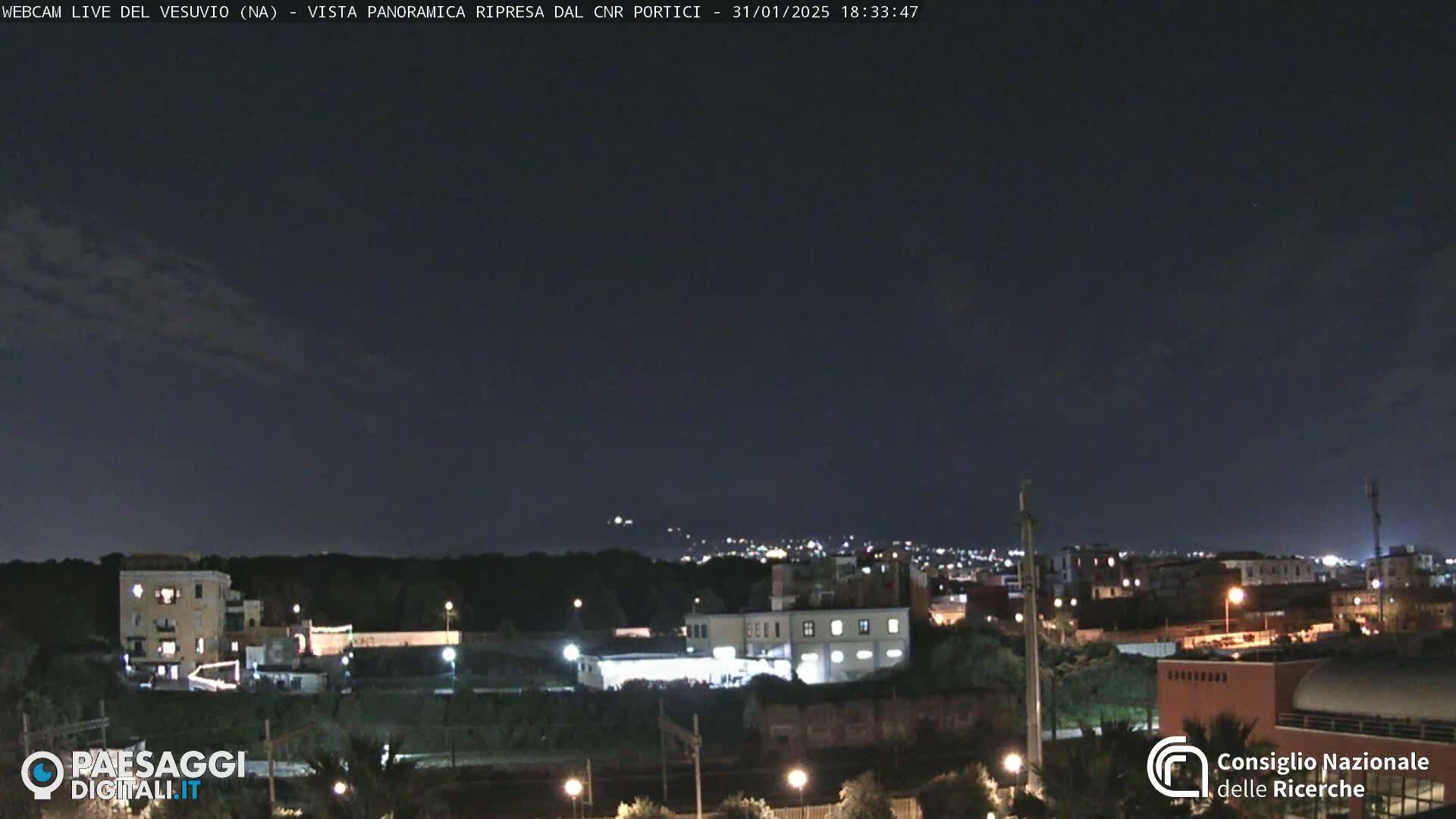 A nighttime, panoramic view of a city illuminated by streetlights under a dark, mostly clear sky.