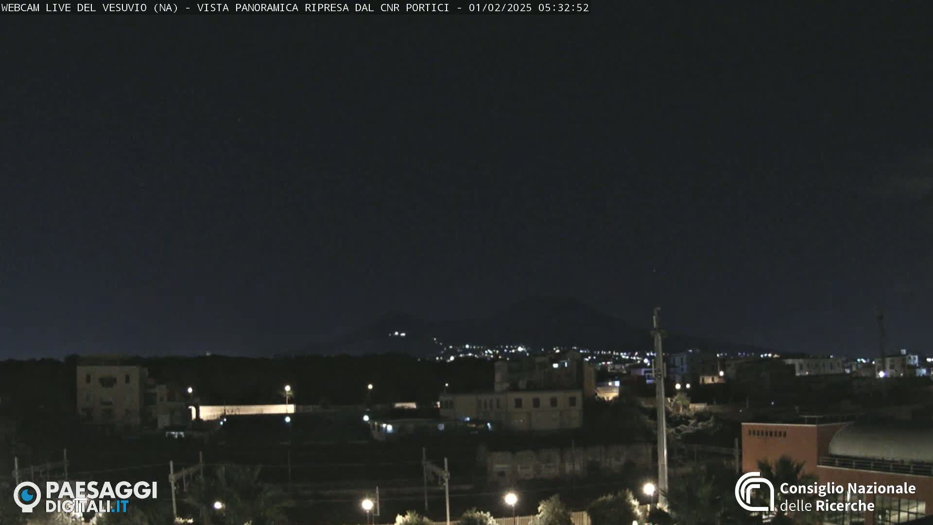 A nighttime view of a city with distant lights and a dark mountain in the background under a clear, dark sky.
