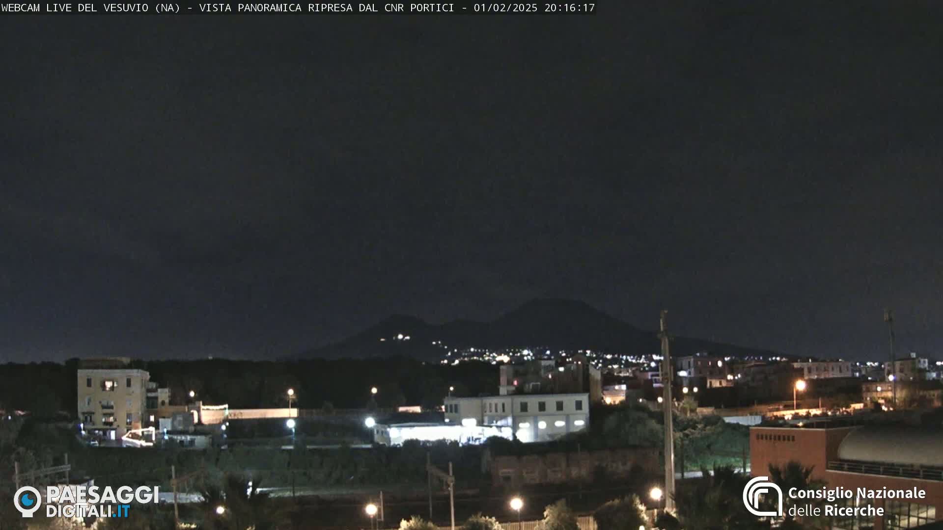 A nighttime view of a city with a volcano in the distance under a clear, dark sky.