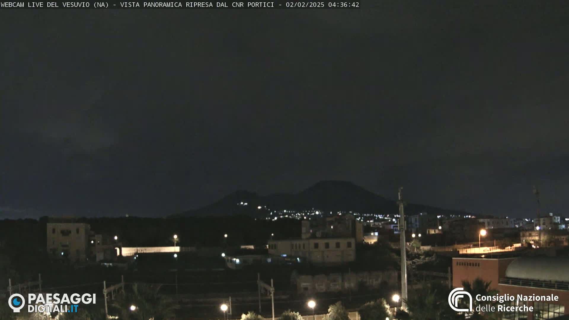 A nighttime view of a city with a volcano in the background under a dark, clear sky.
