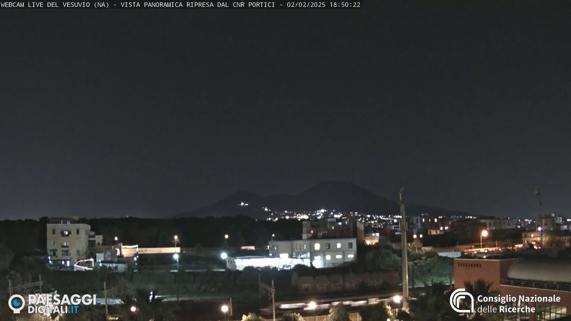 A nighttime view of a city with a distant, dimly lit mountain range under a dark, clear sky.