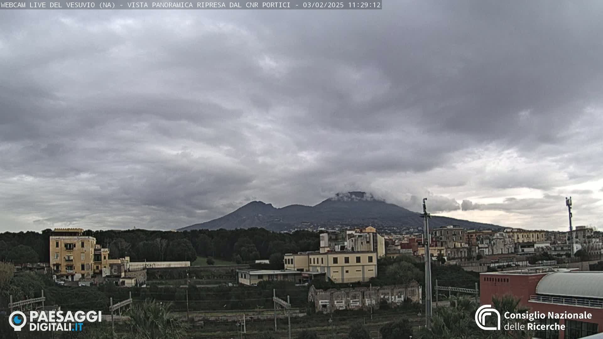 A distant, overcast mountain range is visible above a town with low-rise buildings and sparse vegetation.