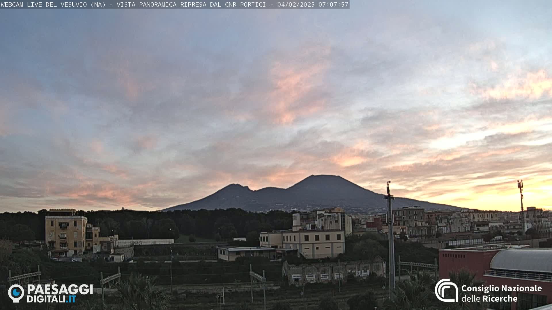 A view of Mount Vesuvius at sunrise, with a pinkish sky and buildings in the foreground.