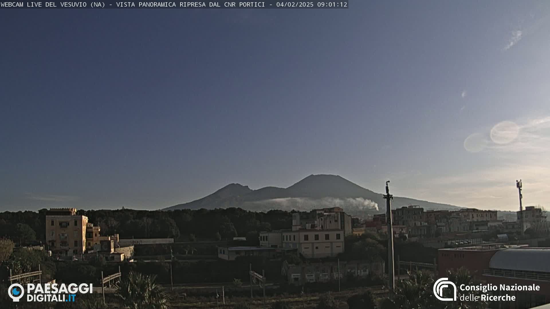 A hazy volcano is visible in the distance above a town under a clear, light-blue sky.