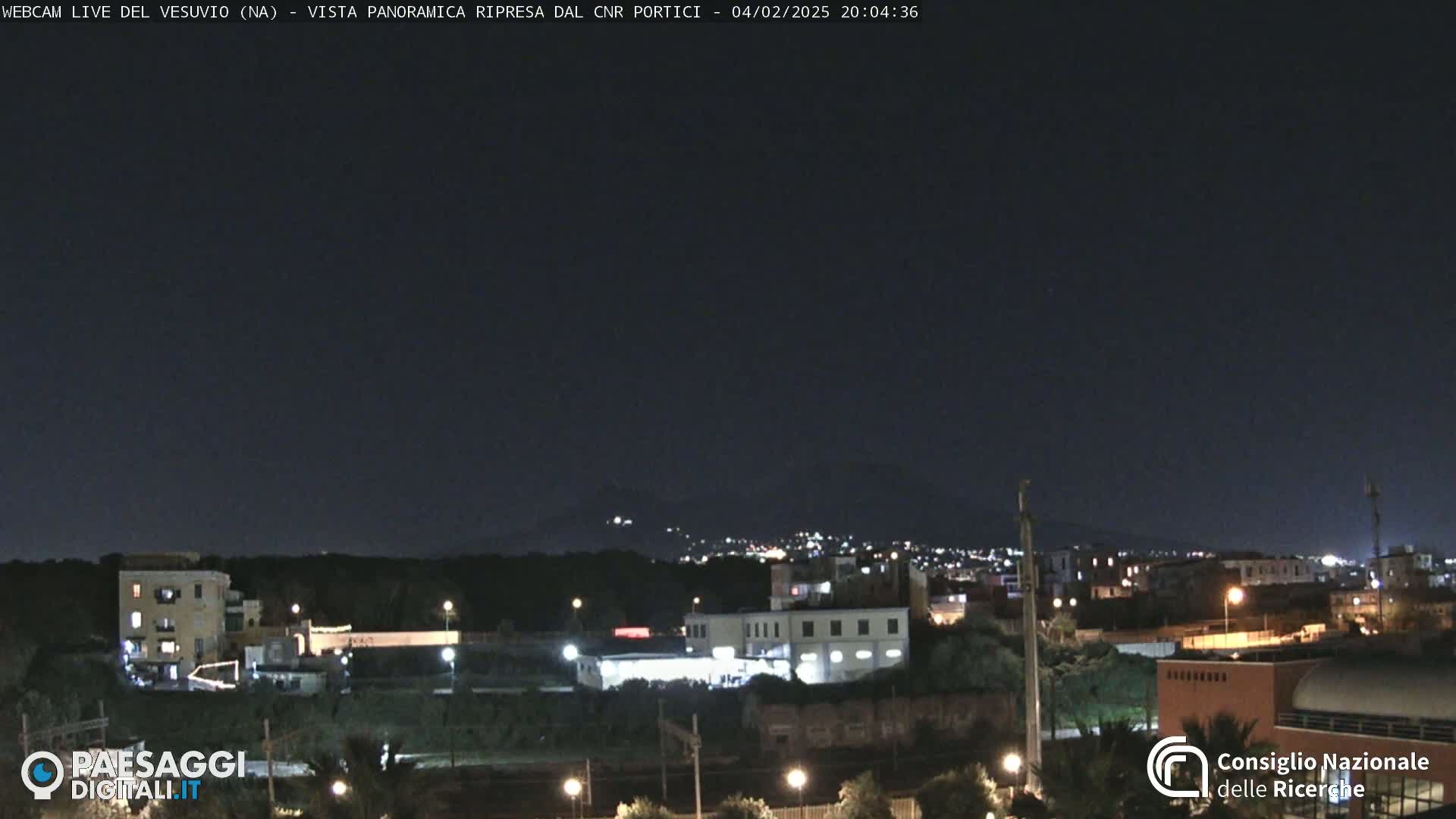 A nighttime view of a town with dimly lit buildings and distant hills under a clear, dark sky.