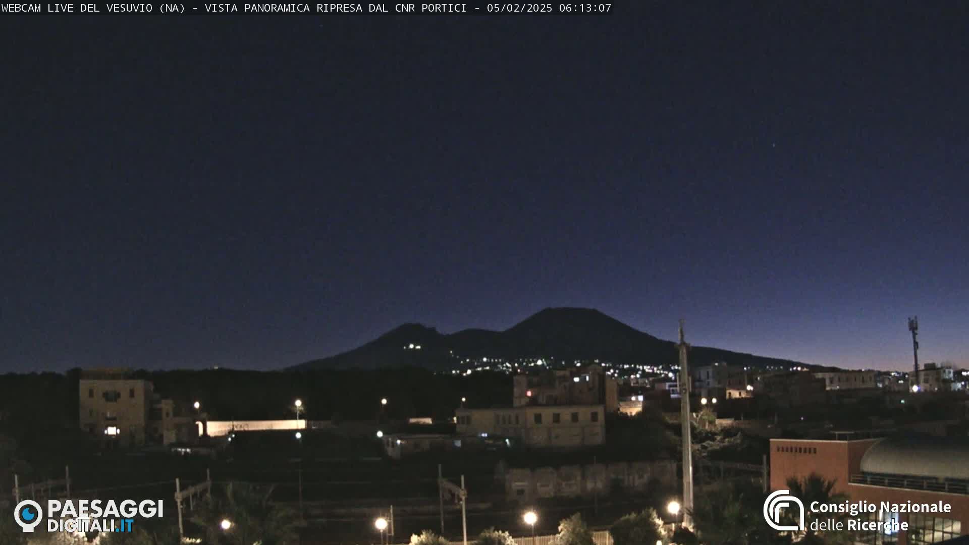 A nighttime view of a city with a volcano in the background under a dark, clear sky.