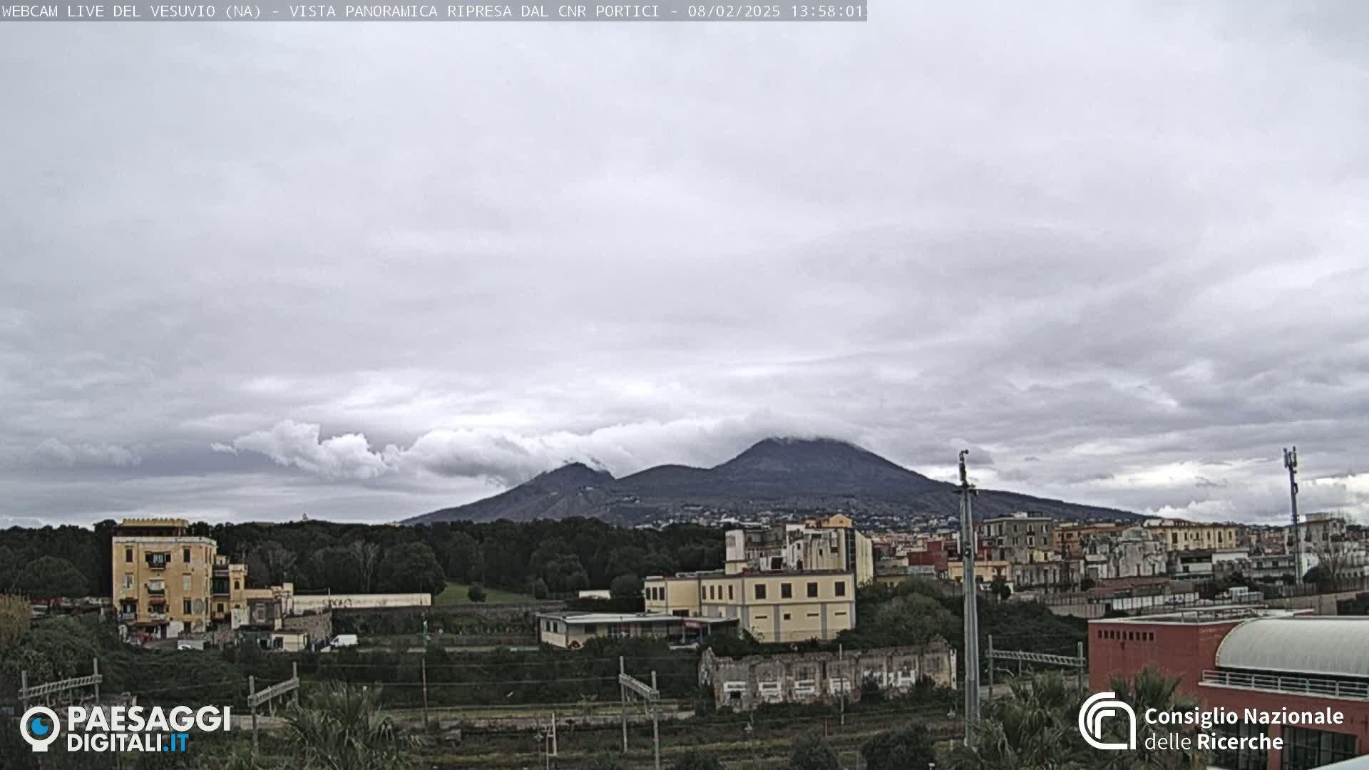 A partly cloudy sky overlooks a town with a distant, partially cloud-covered mountain.