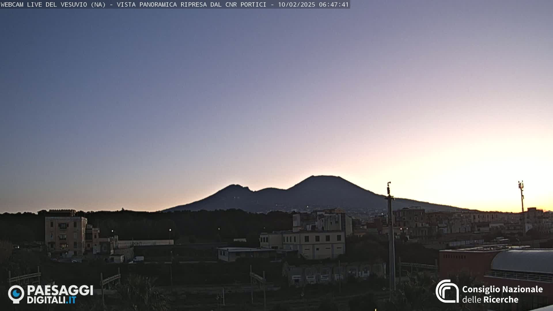 Mount Vesuvius is silhouetted against a twilight sky over a cityscape.