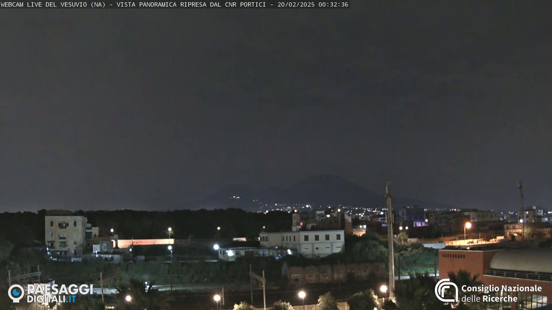 A nighttime view of a city with a dark mountain in the distance under a clear, dark sky.