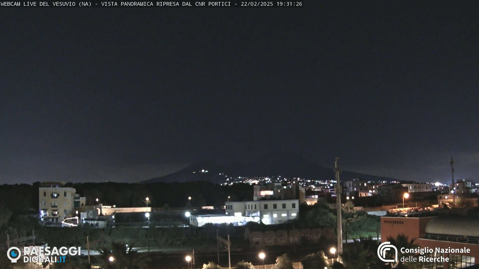 A nighttime view of a city with a volcano in the distance under a clear, dark sky.
