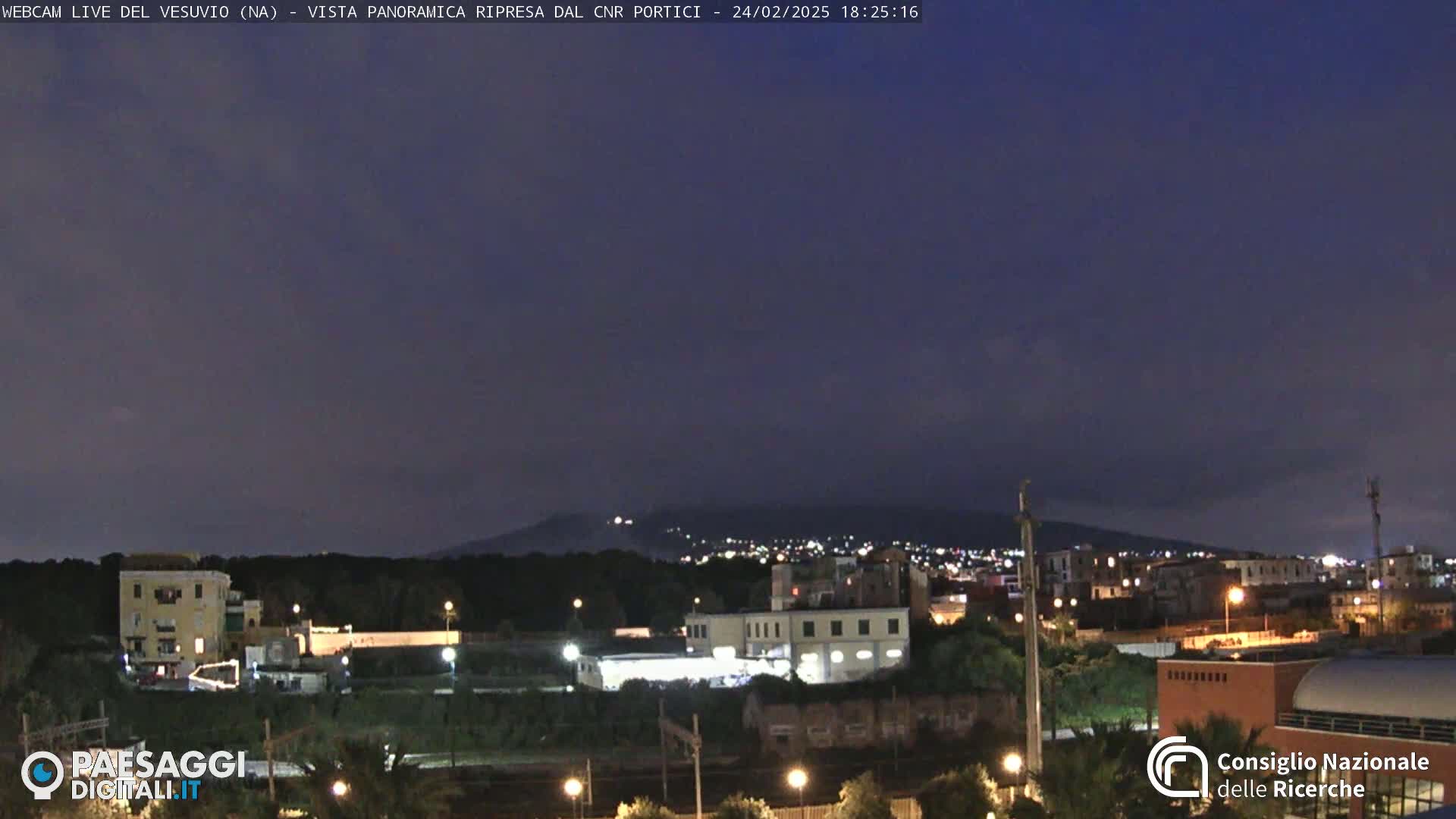 A nighttime, panoramic view of a city with a dark mountain in the background under a clear, dark sky.