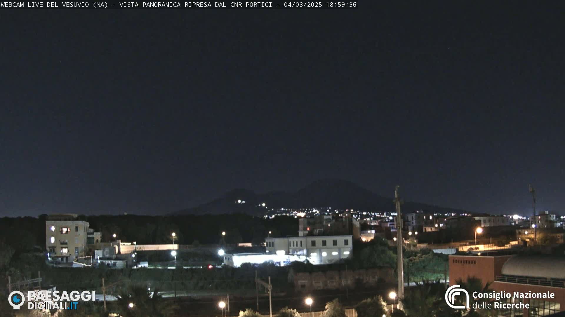 A nighttime view of a city with a volcano in the distance under a clear, dark sky.