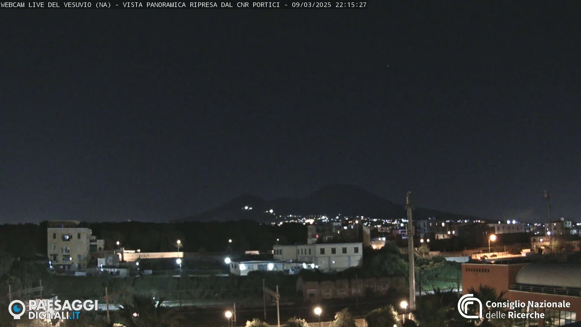 A nighttime view of a town with a distant, dimly lit mountain range under a clear, dark sky.