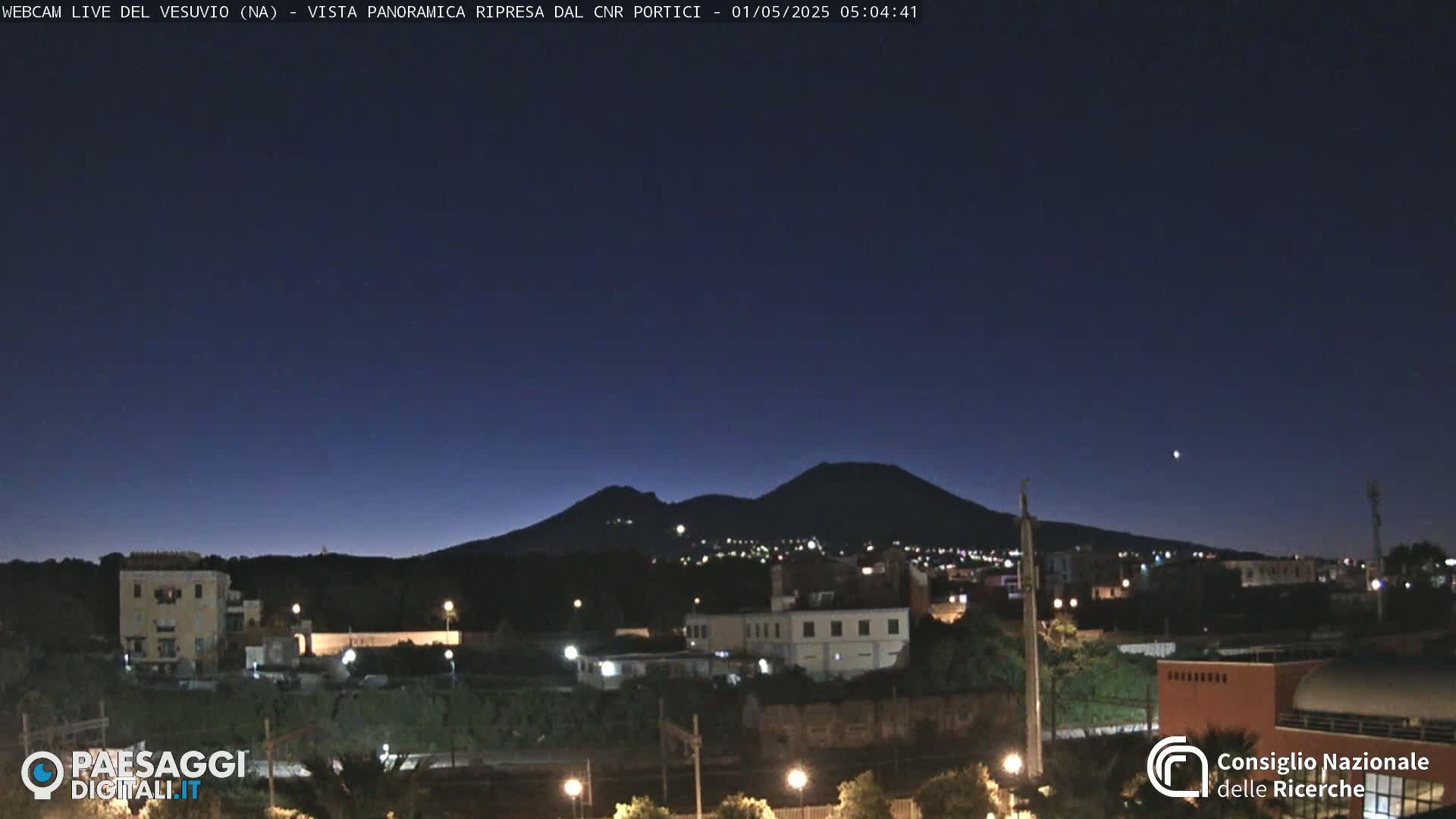 A nighttime, long shot of a city with a volcano silhouetted against a dark blue sky.