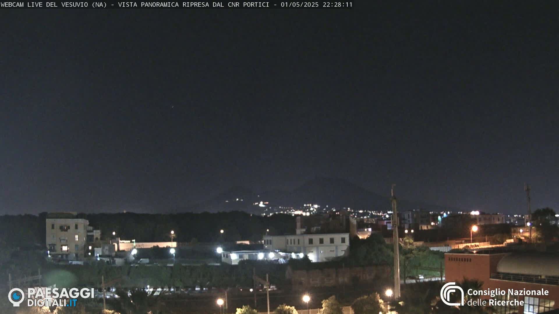A nighttime view of a city with a distant, dimly lit mountain in the background under a clear, dark sky.