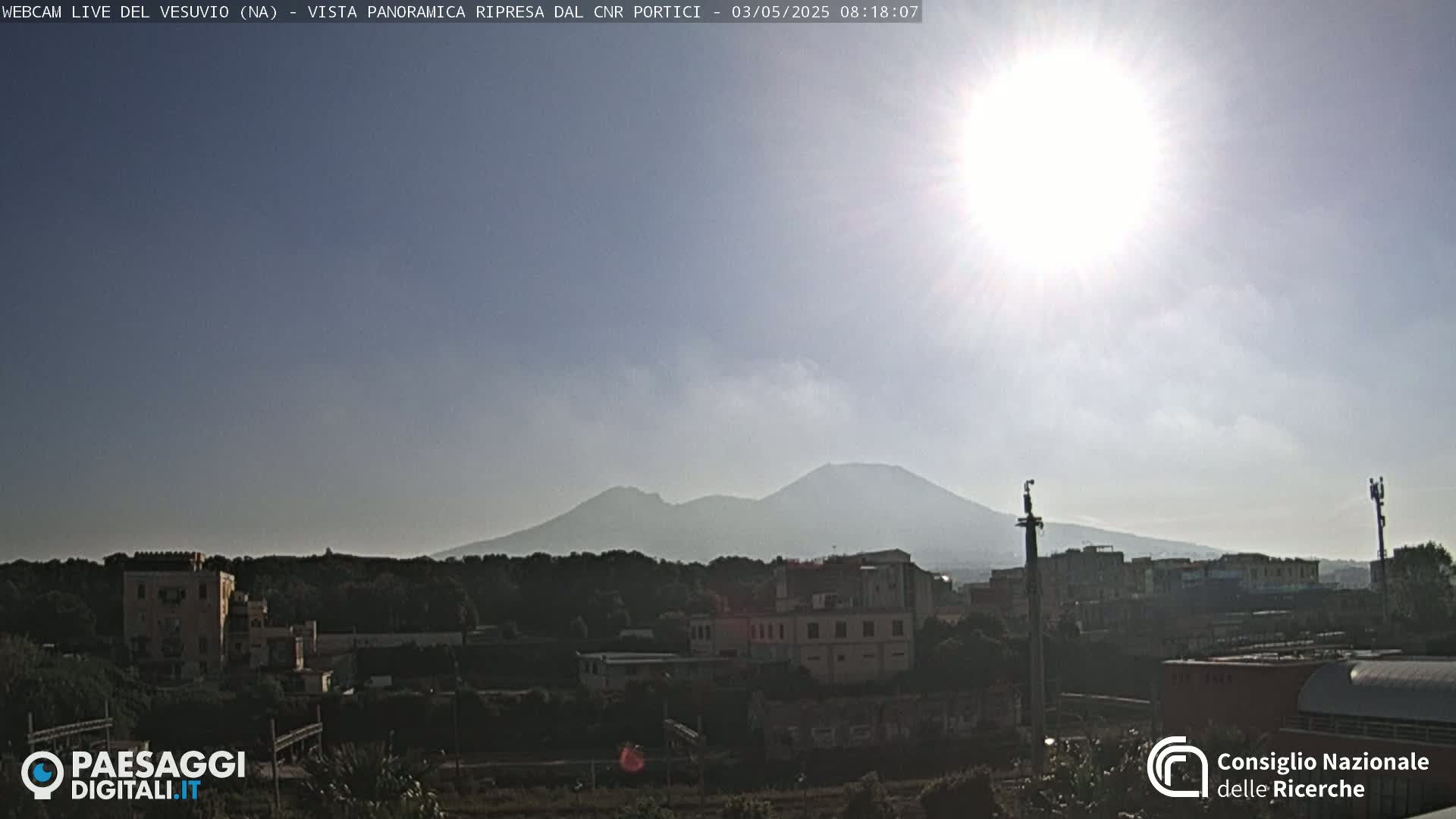 A sunny day reveals a distant, hazy mountain range behind a town of low-rise buildings.