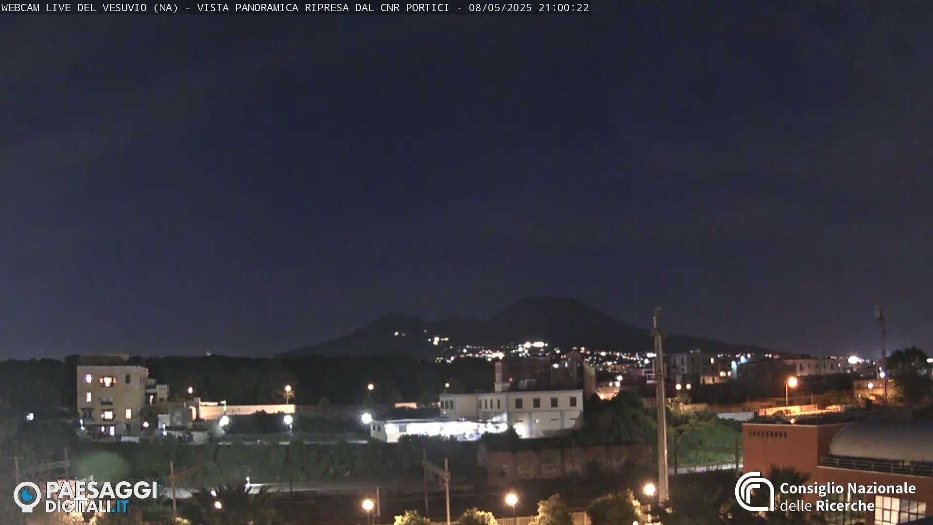 A nighttime view of a city with a volcano in the distance under a clear, dark sky.