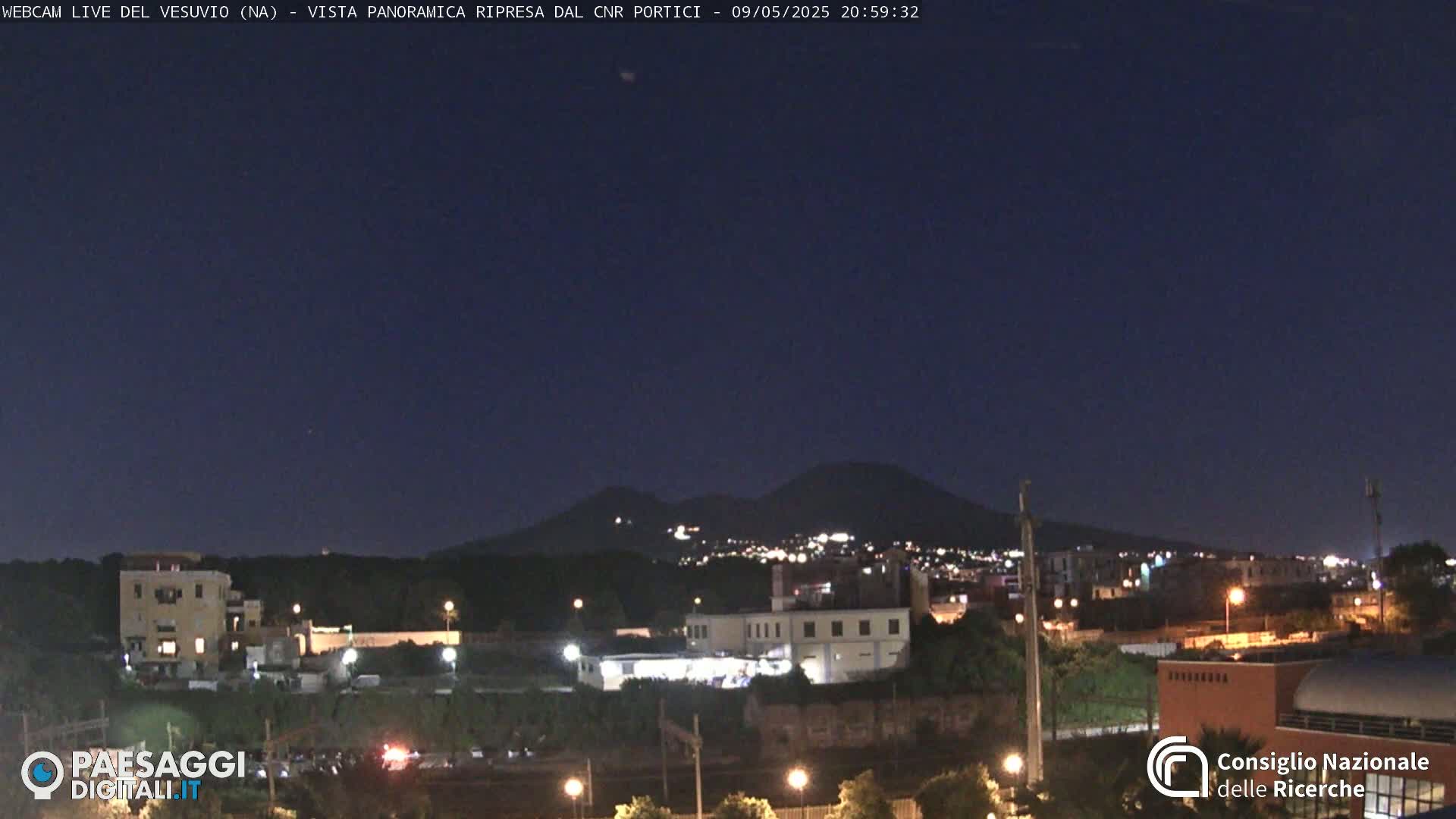 A nighttime view of a city illuminated below a dark, clear sky with a mountain range in the distance.