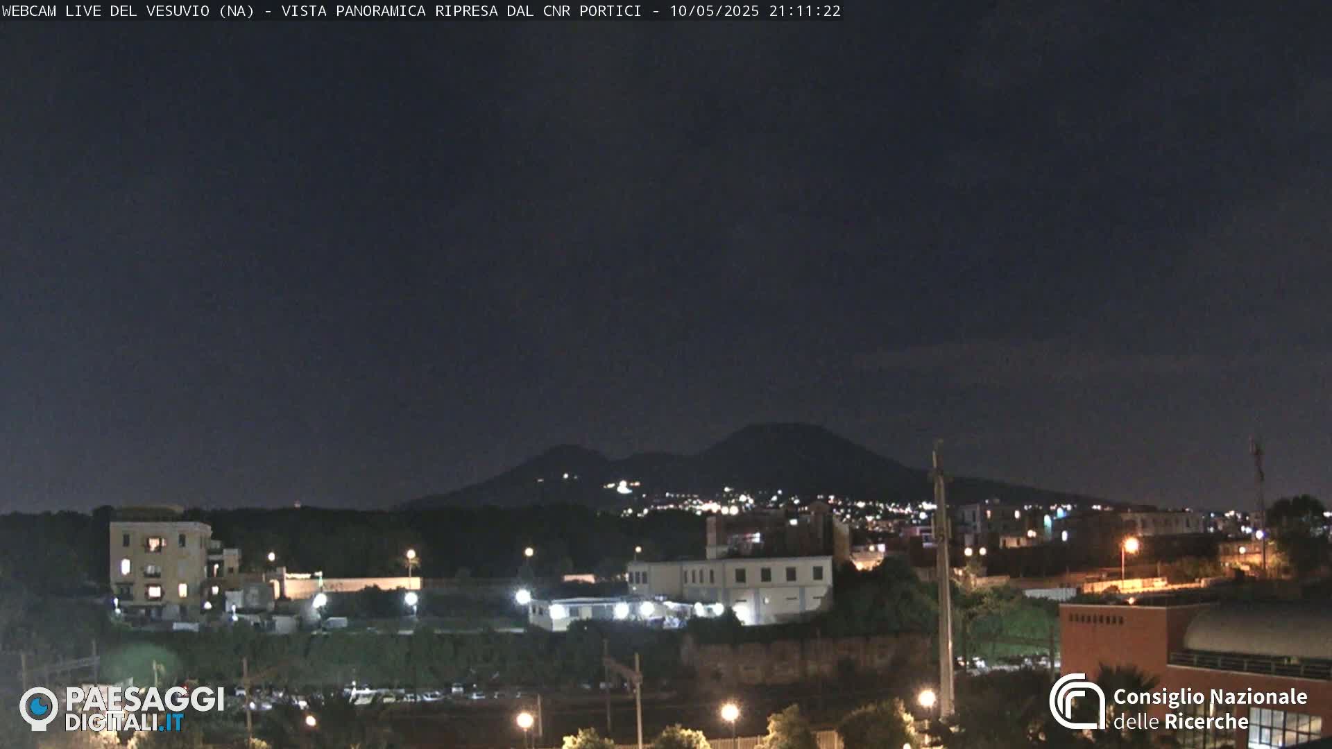 A nighttime view of a city with a volcano in the background under a dark sky.