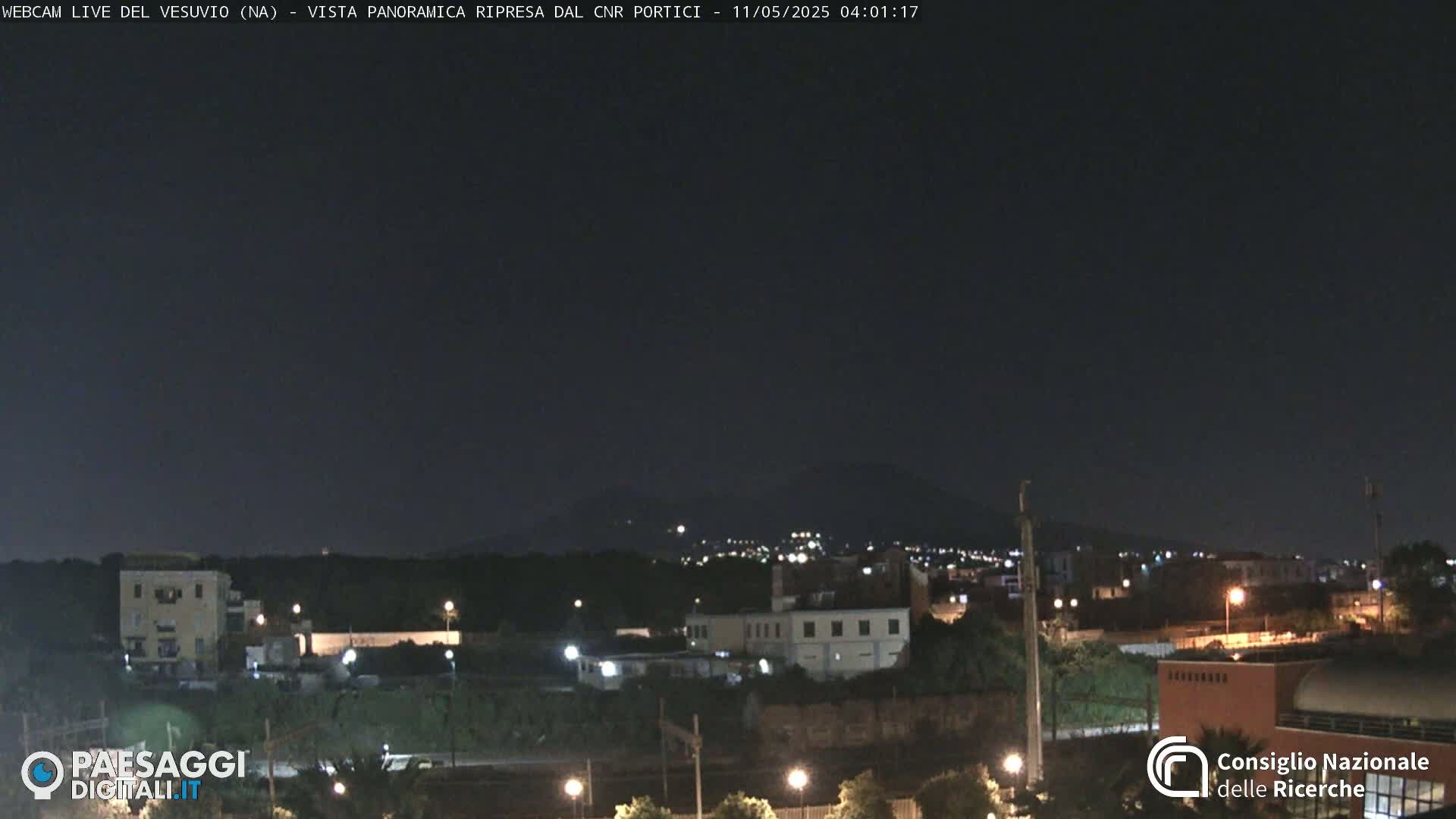 A nighttime, panoramic view of a city with a distant, dark mountain range under a clear, dark sky.