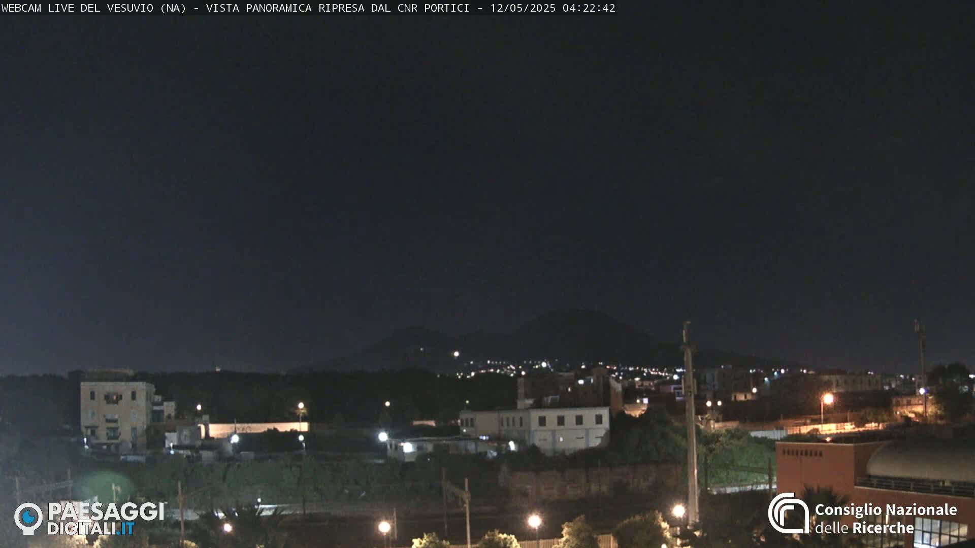 A nighttime view of a town with a distant mountain range under a dark, clear sky.
