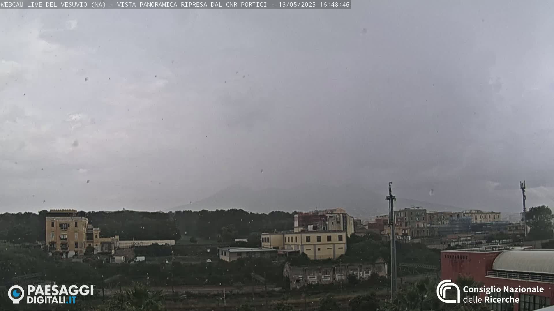 A distant, hazy mountain is visible behind a town experiencing light rain or snow.