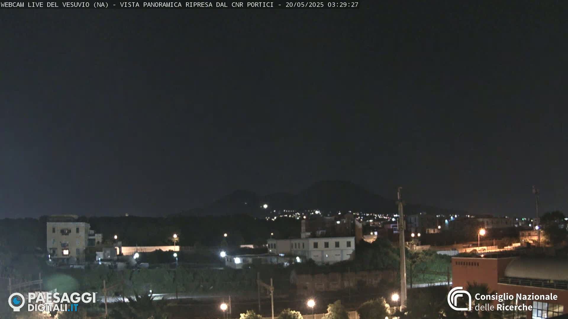 A nighttime, long shot of a city with a mountain range in the distance under a clear, dark sky.