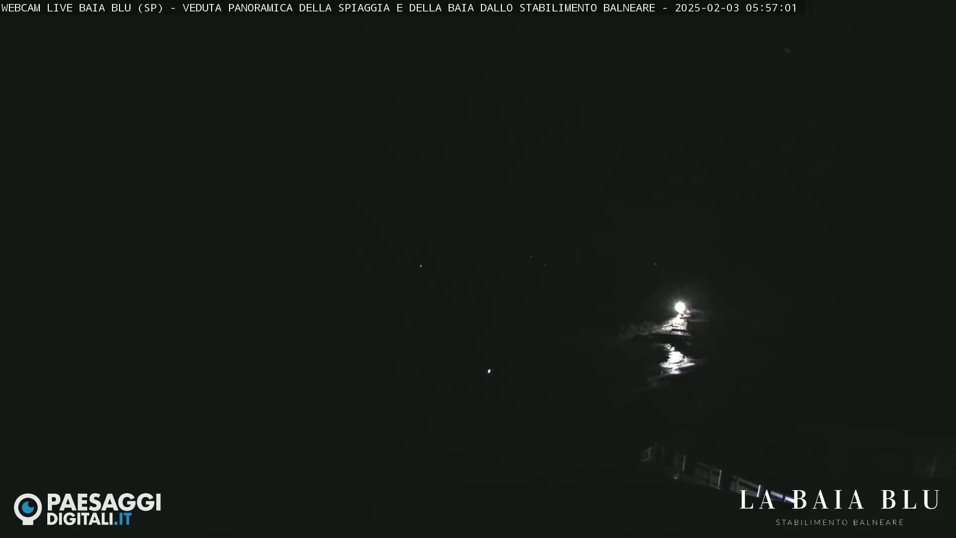 A dark nighttime scene shows a body of water reflecting a bright light source in the distance.