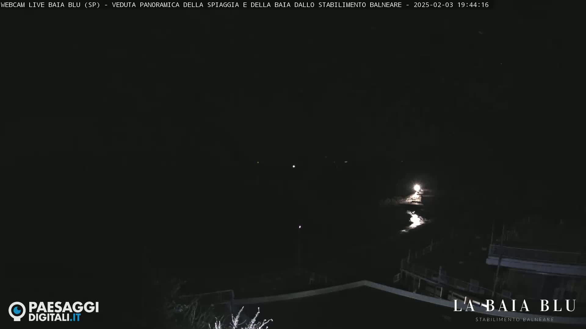 A nighttime, panoramic view of a dark bay with a few faint lights visible along the shoreline.