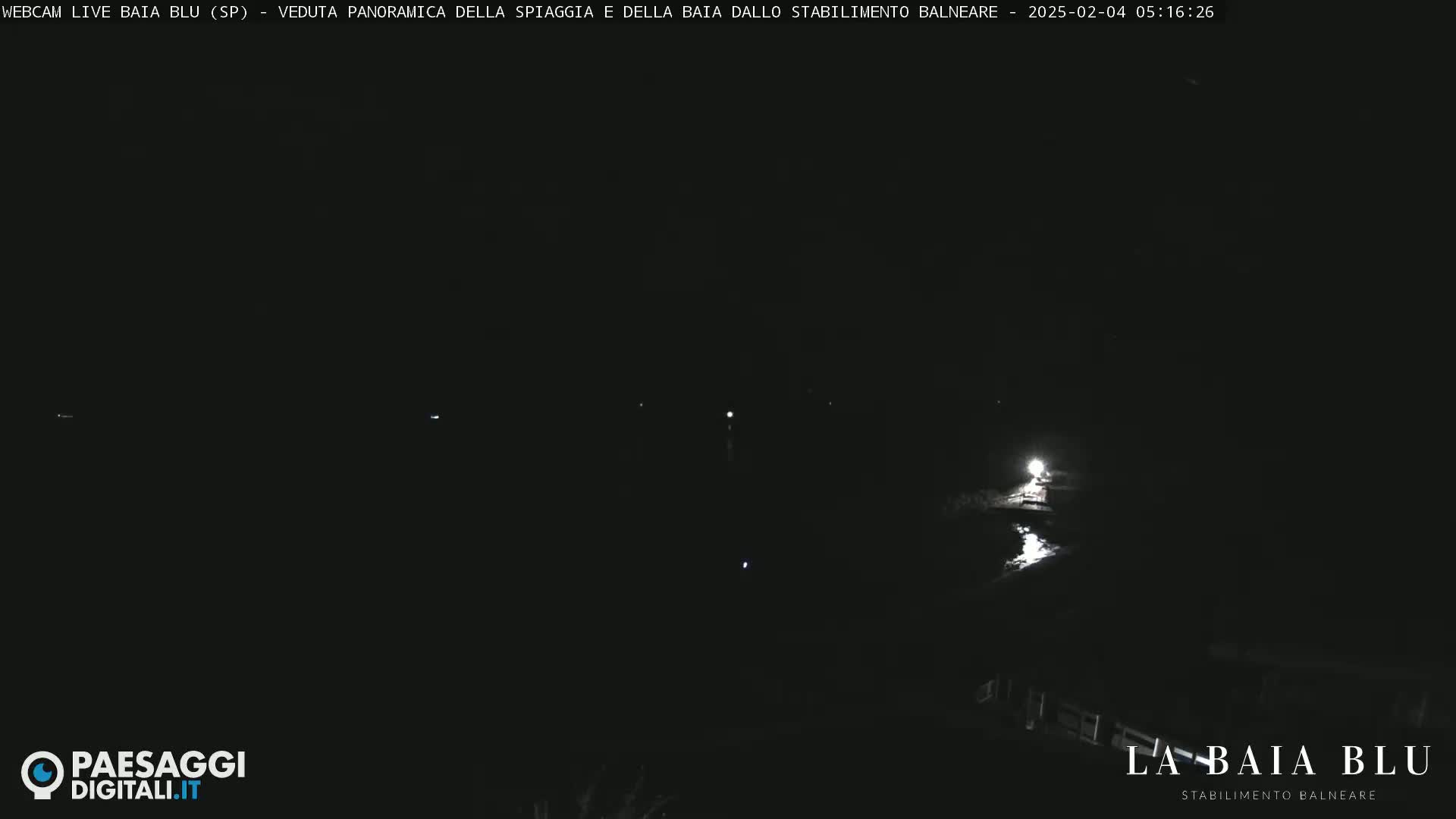 A nighttime, dark panoramic view of a beach and bay, illuminated only by a few faint lights.