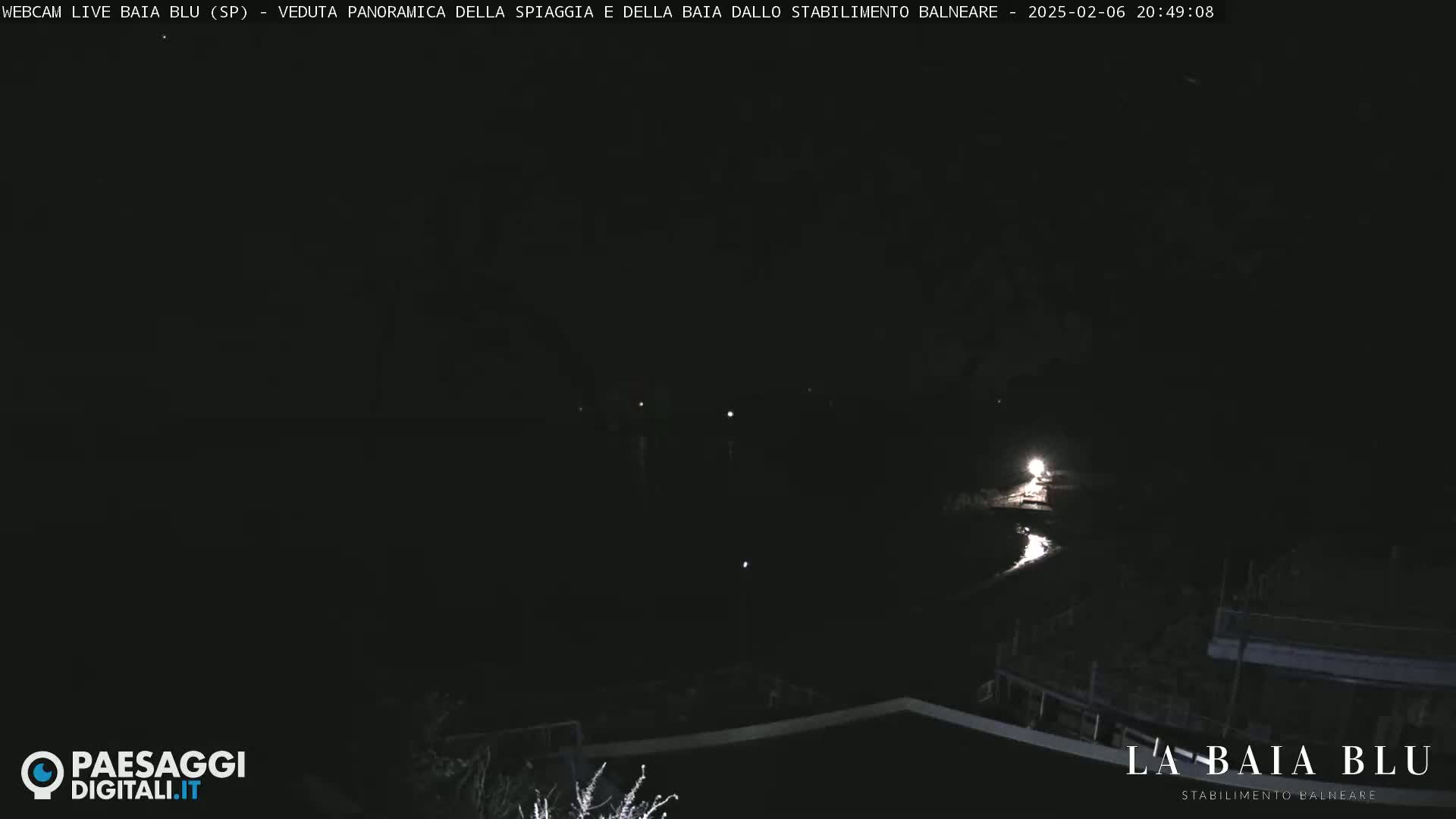 A nighttime, panoramic view of a dark beach and bay, illuminated by a few distant lights.