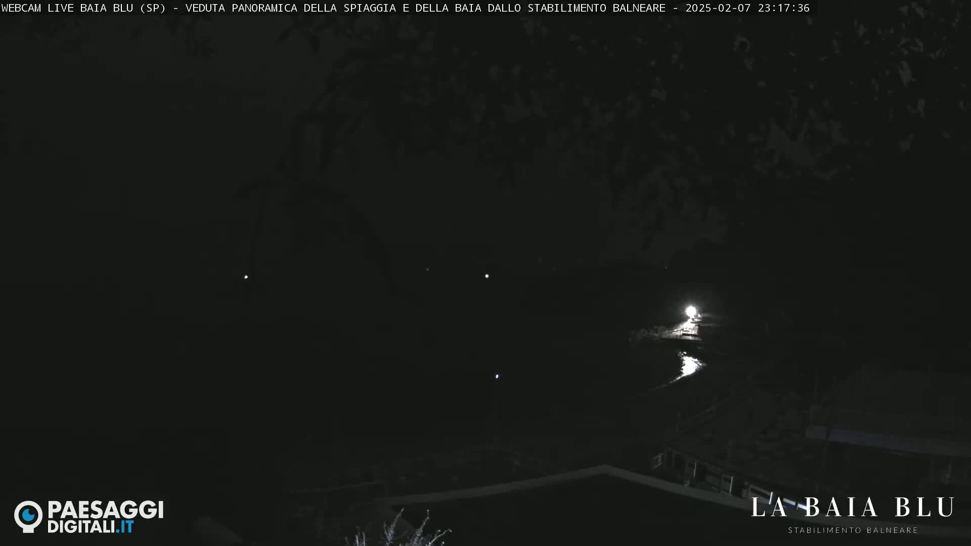 A nighttime, dark view of a beach and bay from a distance, with a few faint lights visible.