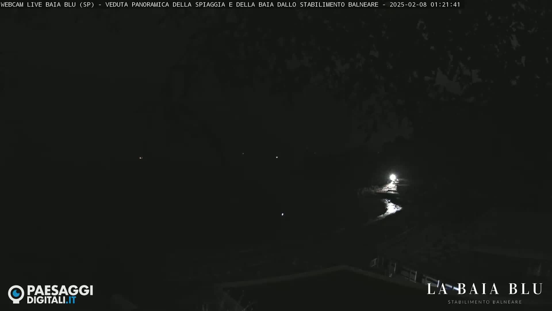 A nighttime, dark panoramic view of a beach and bay, lit faintly by a single light source.