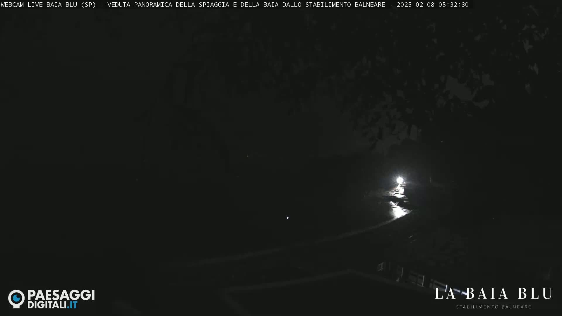 A nighttime, low-light view of a dark, possibly wet, paved area with a single bright light source in the distance.