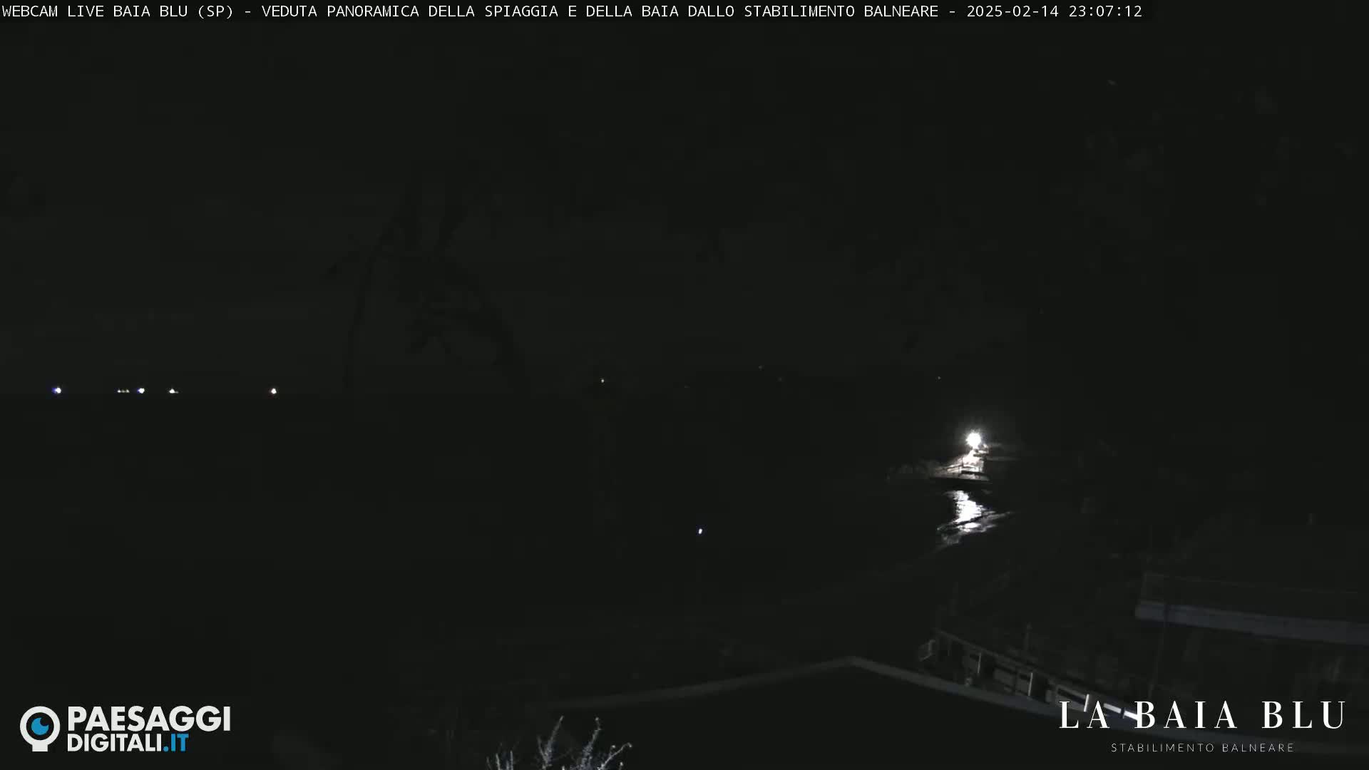 A dark nighttime scene shows a dimly lit shoreline with a few faint lights in the distance.