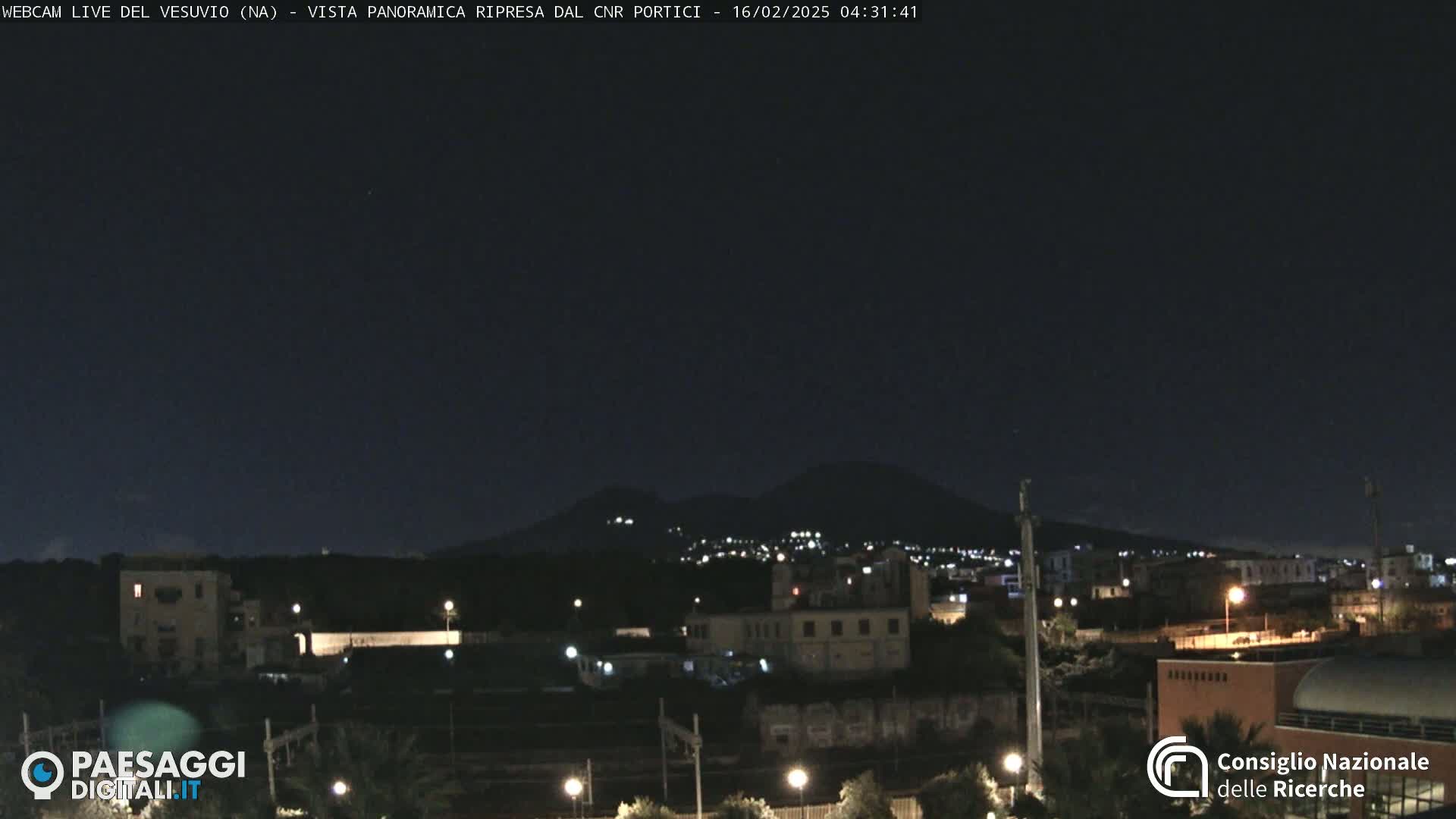 A nighttime view of a city with a distant, dimly lit mountain range under a clear, dark sky.