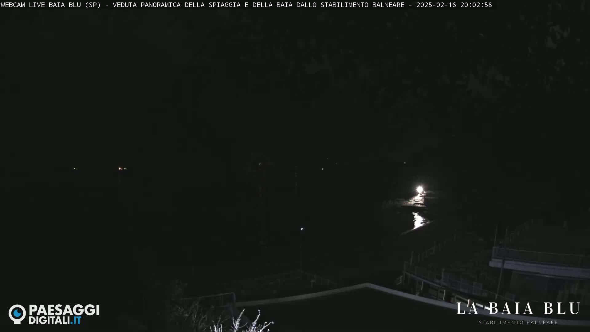 A dark nighttime scene shows a dimly lit beach and body of water.