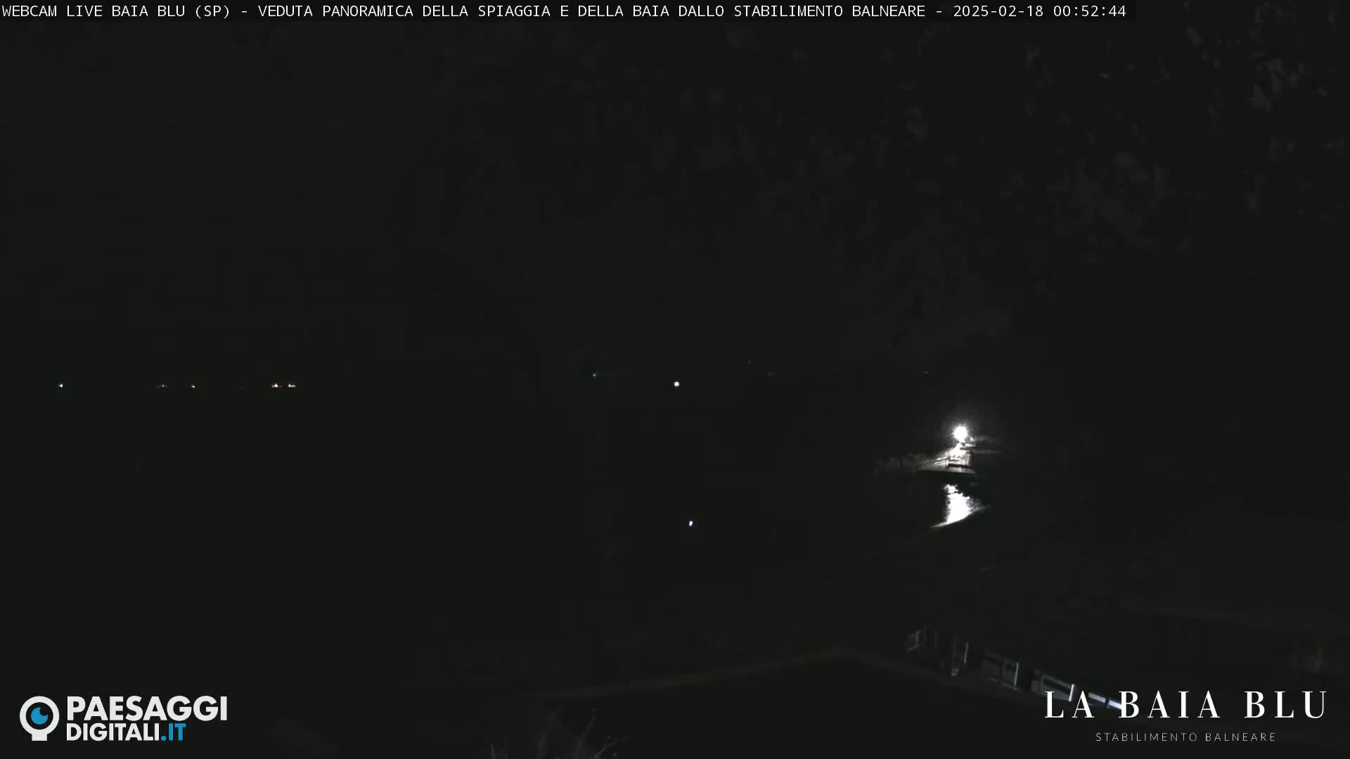 A nighttime, panoramic view of a dark beach and bay with a few distant lights visible.