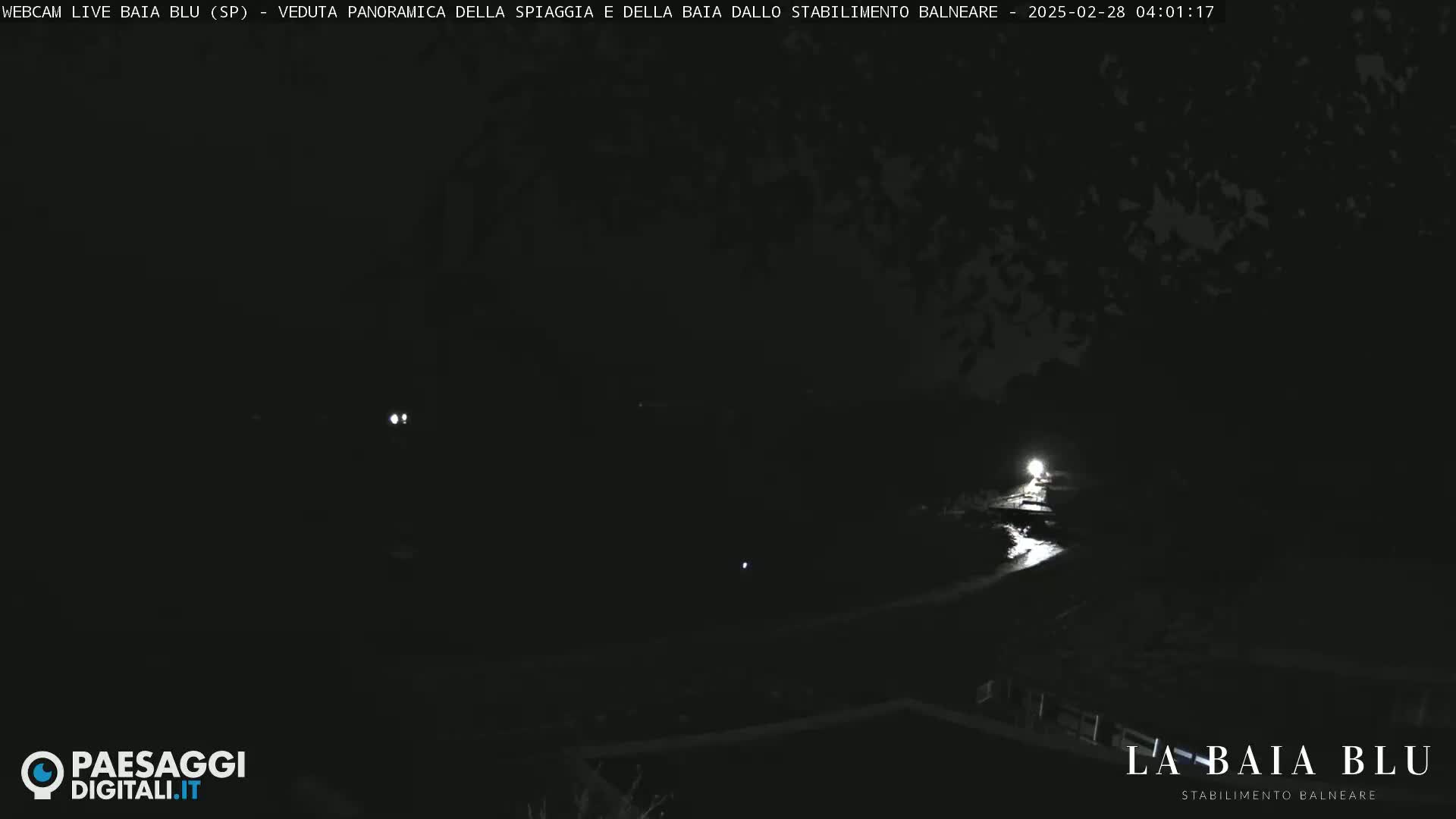 A dark nighttime scene shows a dimly lit path or road leading to a brighter area, possibly a light source.