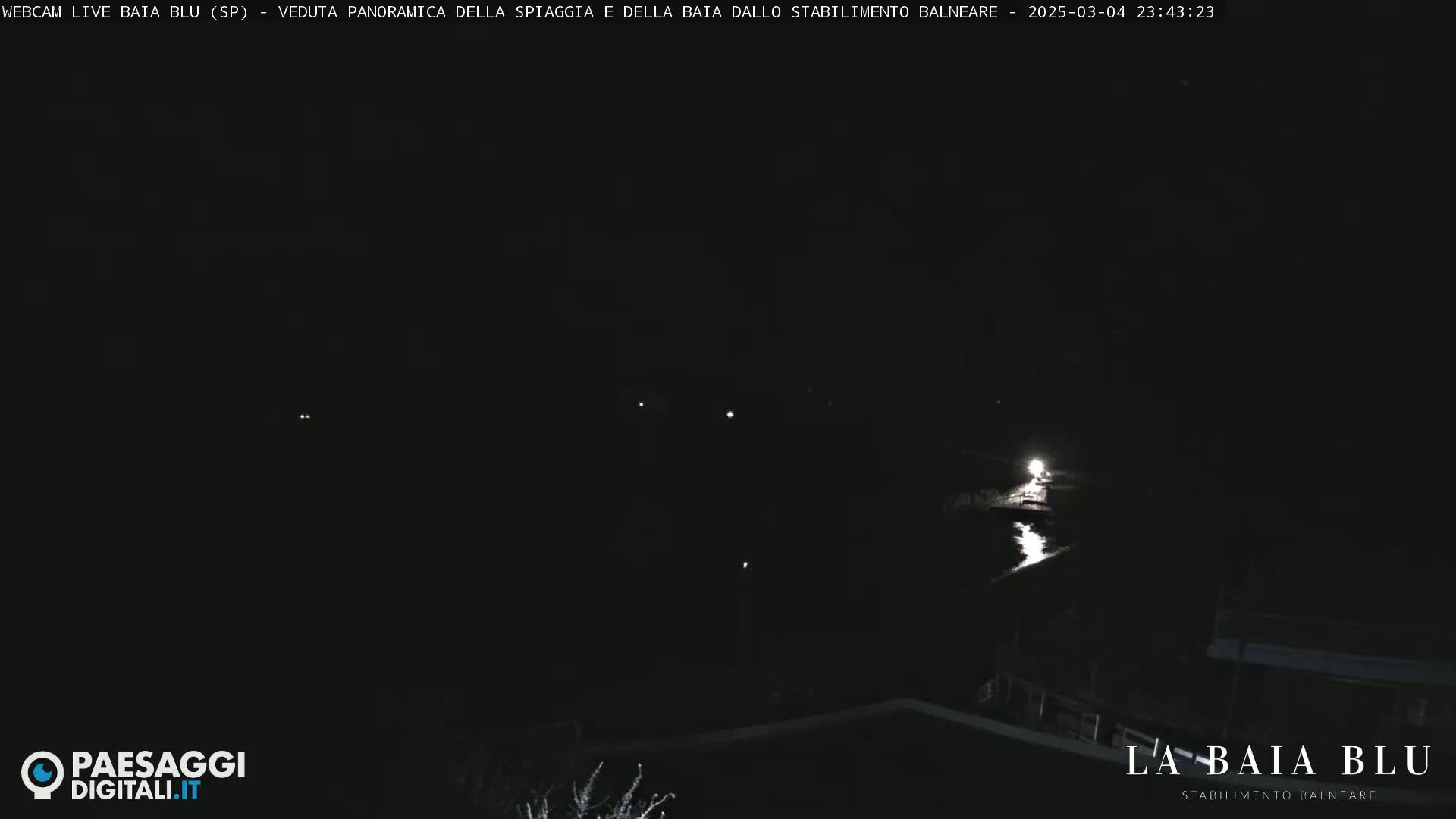 A dark nighttime scene shows a body of water reflecting light, with a few distant lights visible on the land.