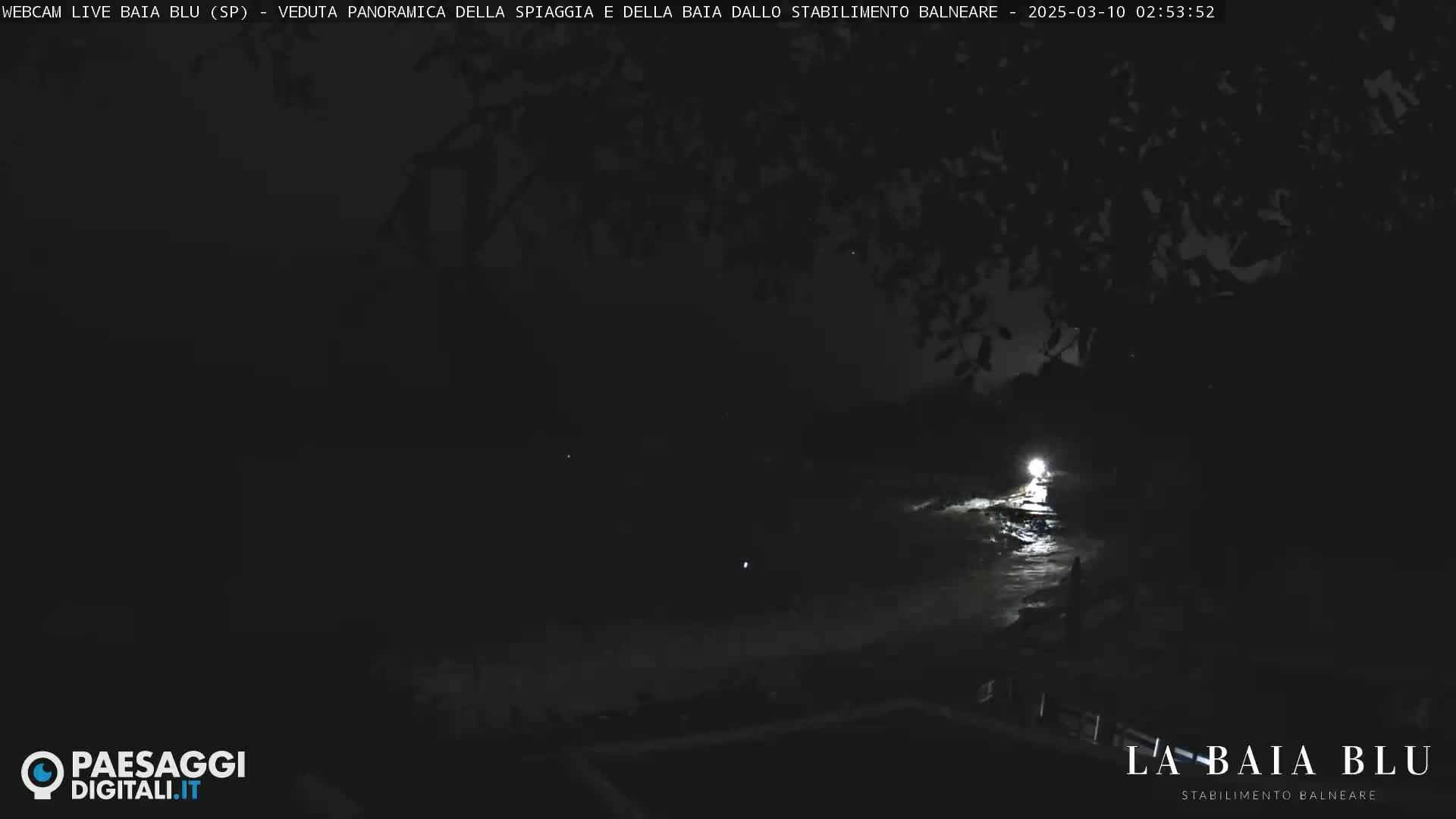 A nighttime, dark view of a beach with a single bright light visible near the water's edge.