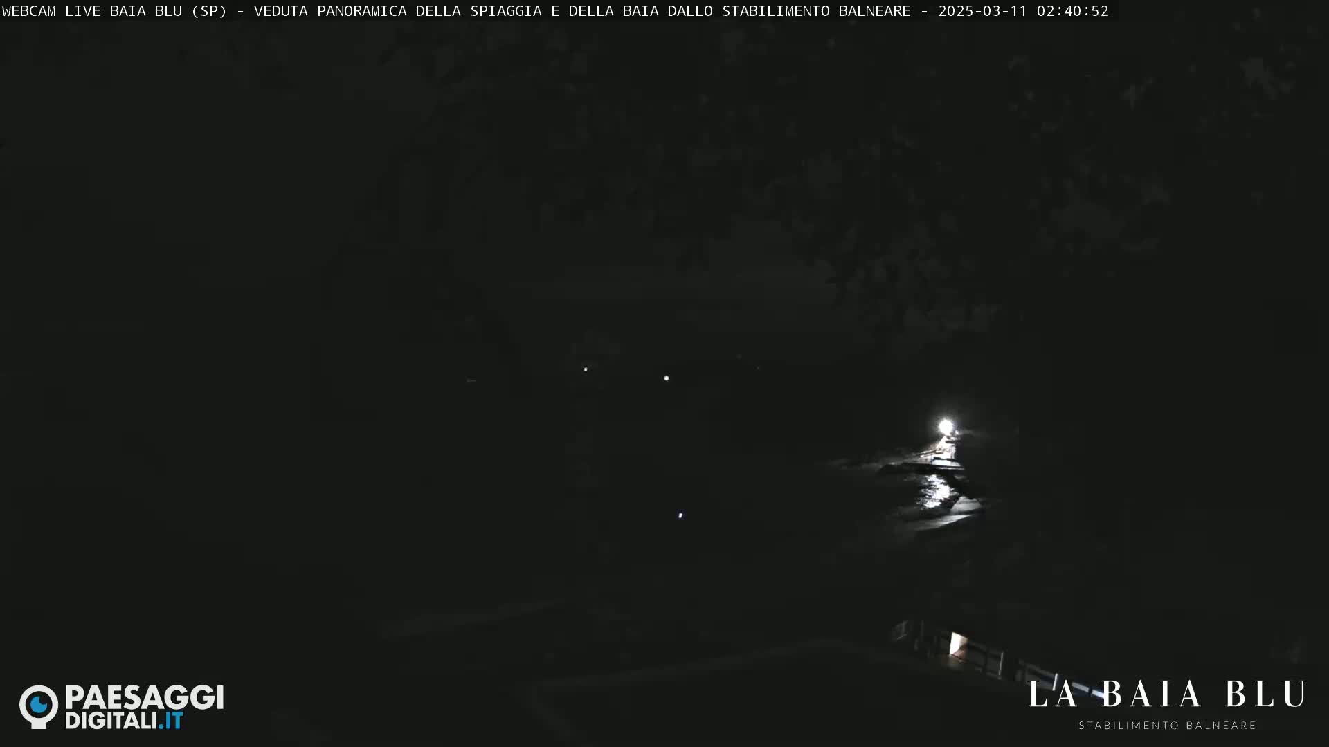A dark, nighttime view of a beach and bay, lit by a single bright light source.
