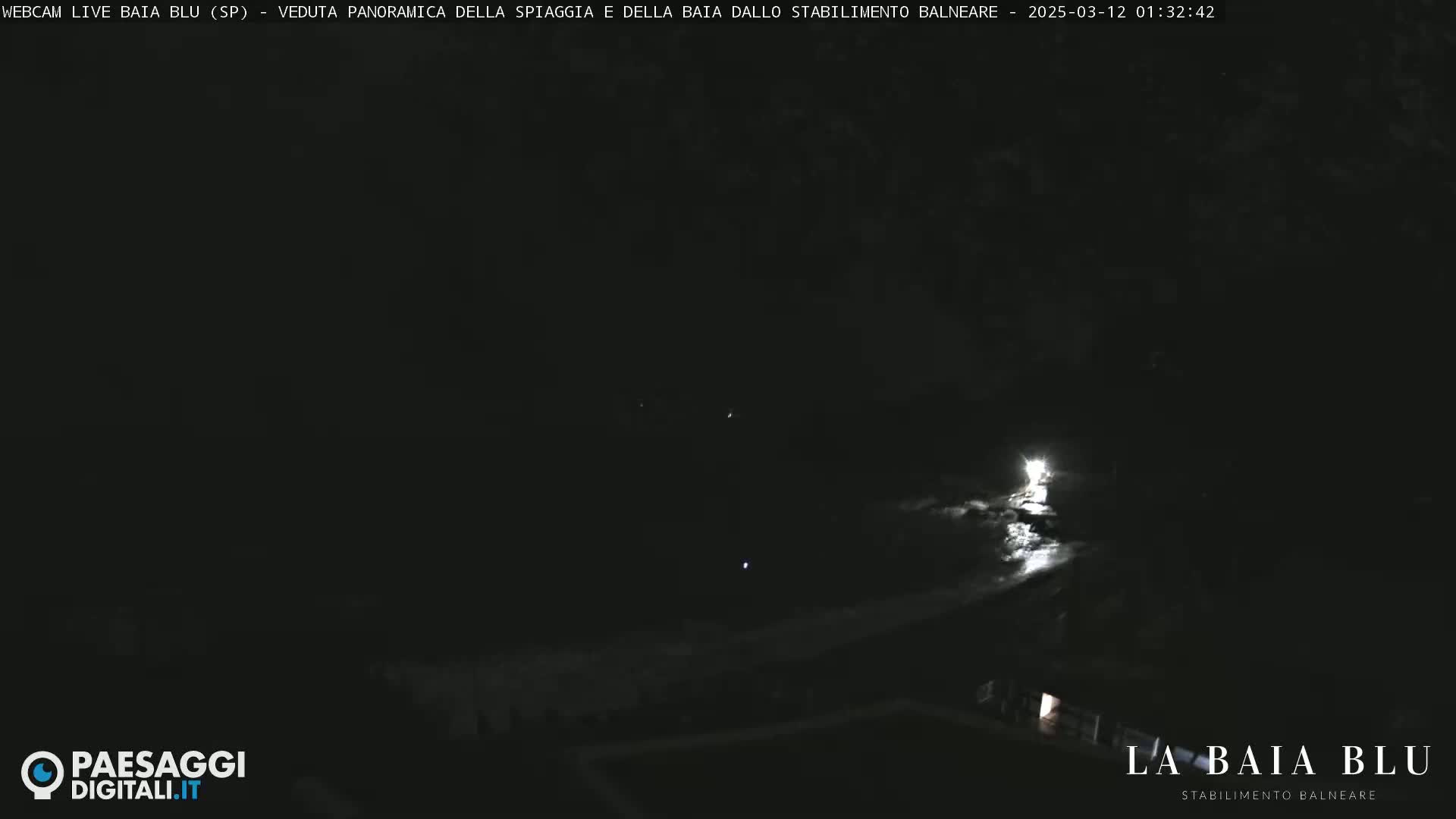A nighttime, dark, and mostly featureless view of a beach from a distance, with a few faint lights visible.